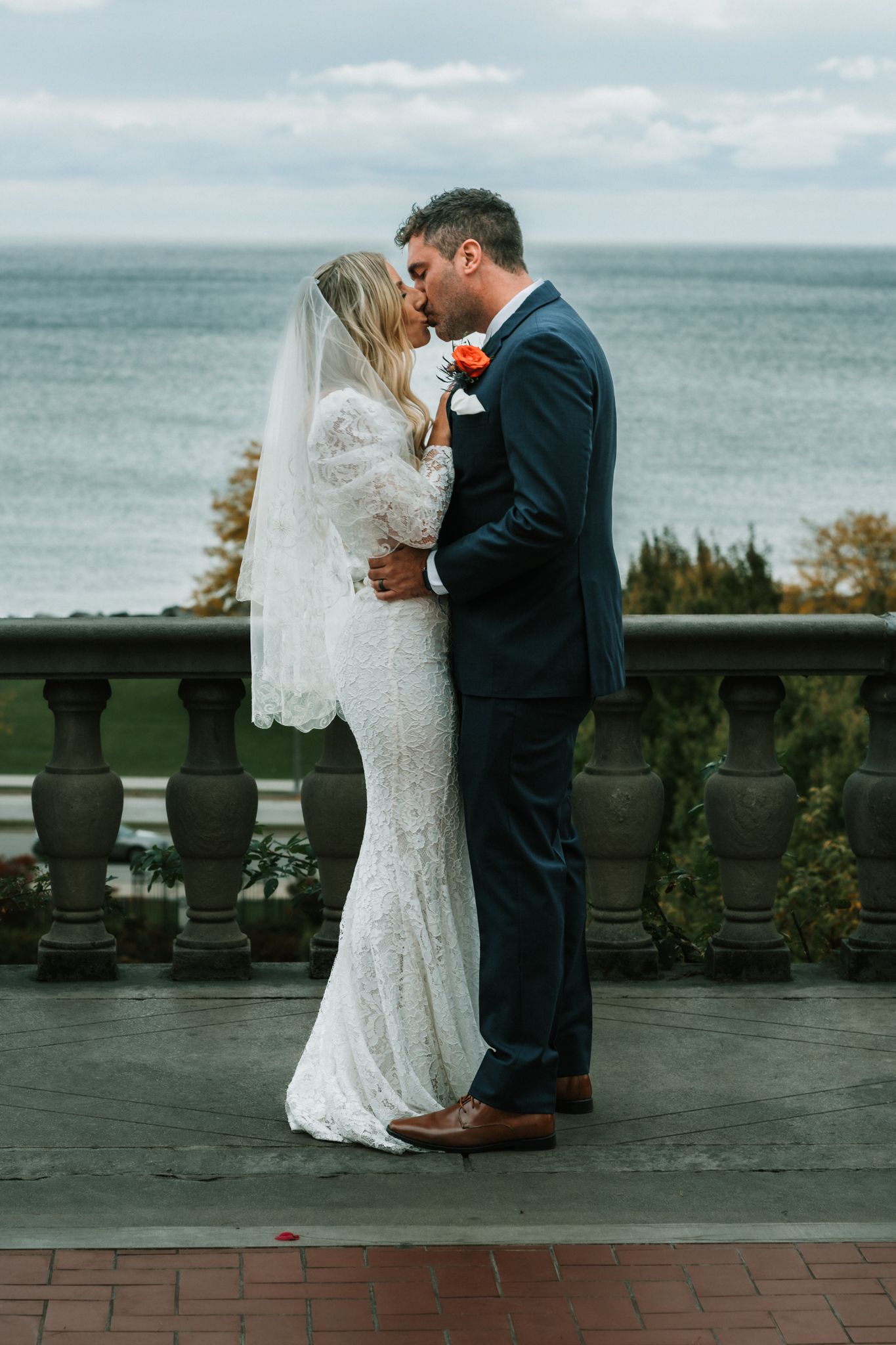 A romantic wedding portrait of a couple kissing on a balcony overlooking the ocean.