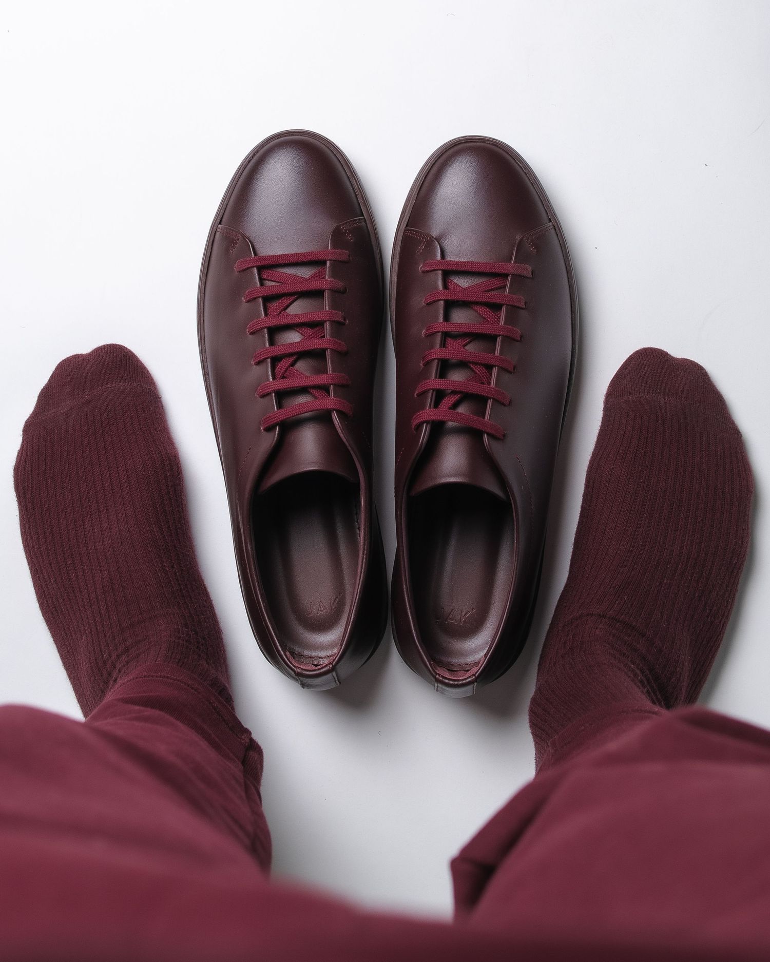 Burgundy leather sneakers with red laces displayed with matching socks on white background.