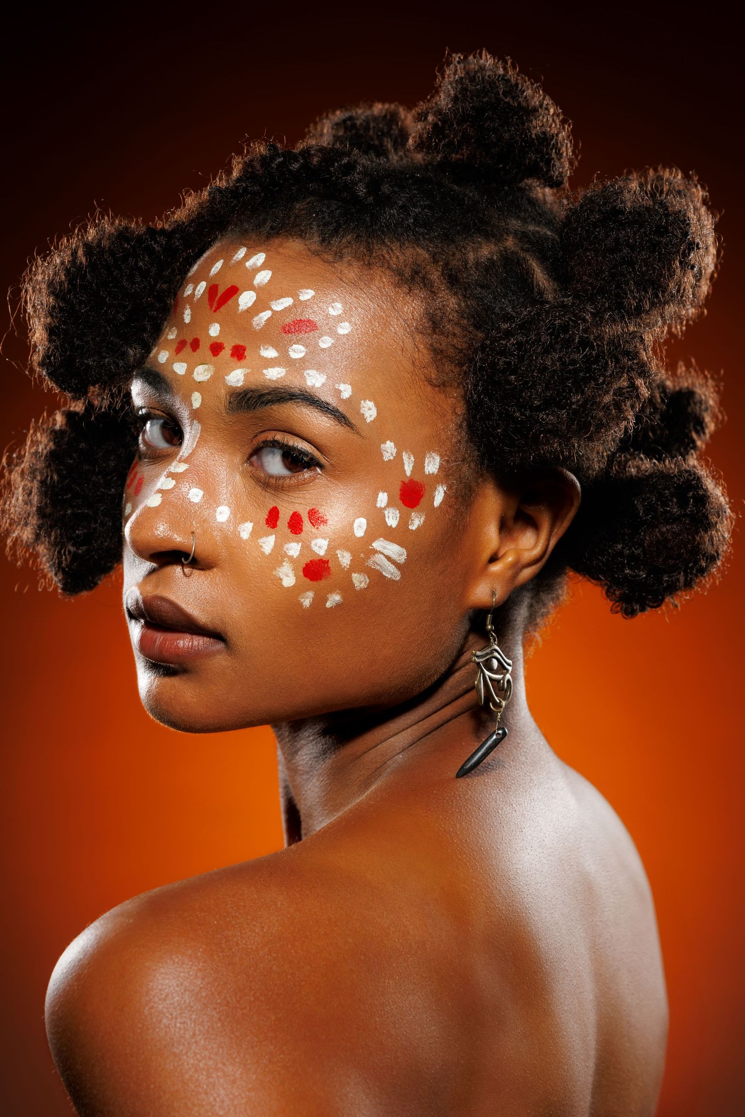Creative portrait with white and red face paint designs against an orange background.