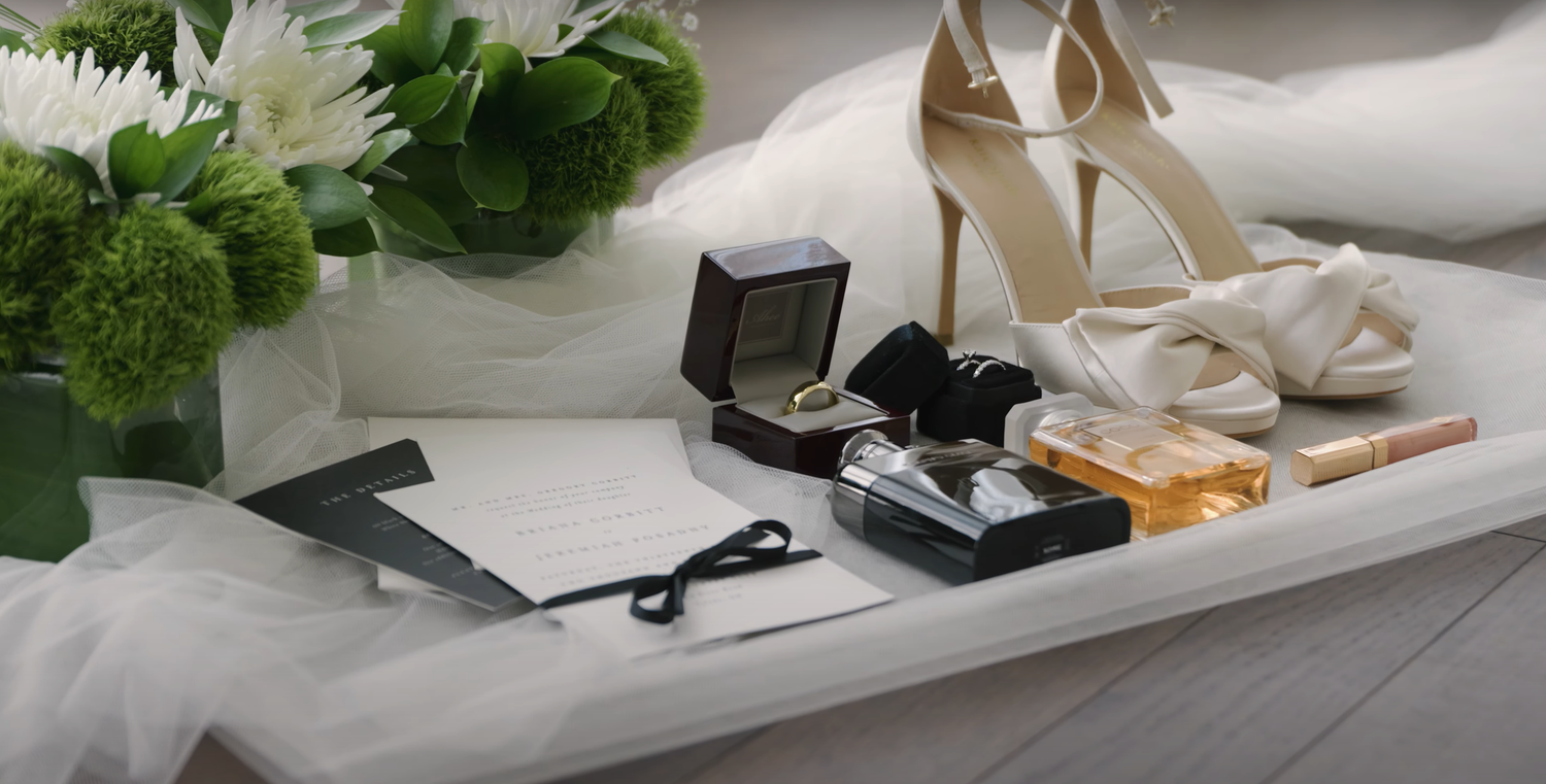 Wedding accessories including white heels, rings in box, and floral decorations arranged on white surface.
