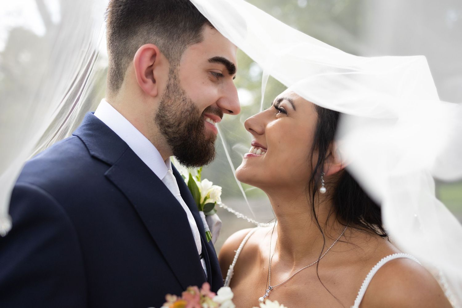 A bride and groom share an intimate moment under flowing white veil.