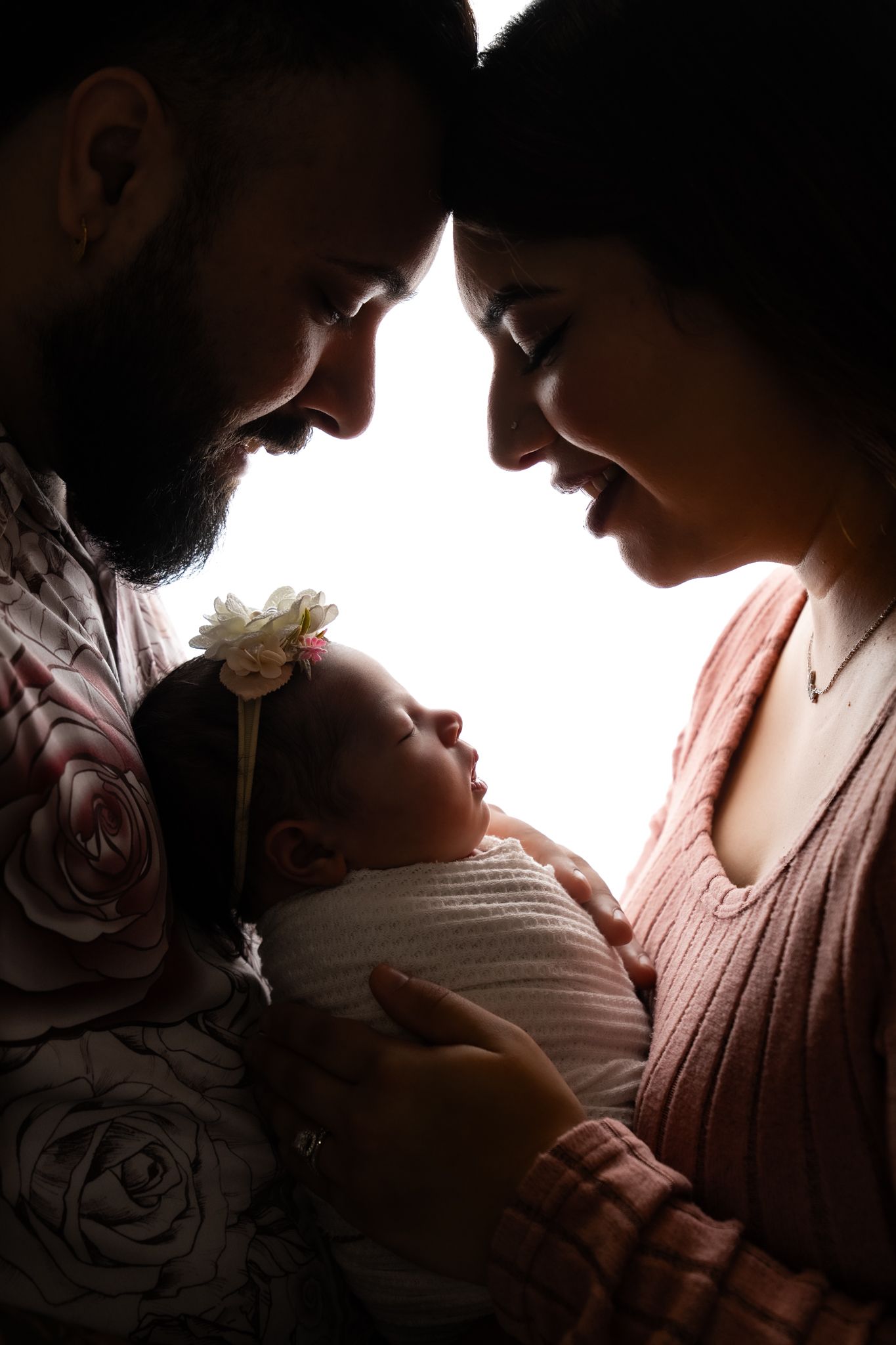 A series of intimate silhouettes capture tender moments between parent and newborn in warm, backlit glow.