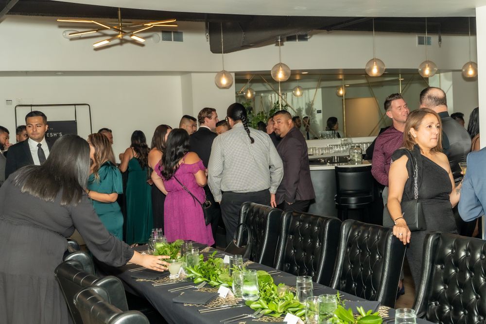 Guests gather around an elegant dining table with green centerpieces at an upscale restaurant event.