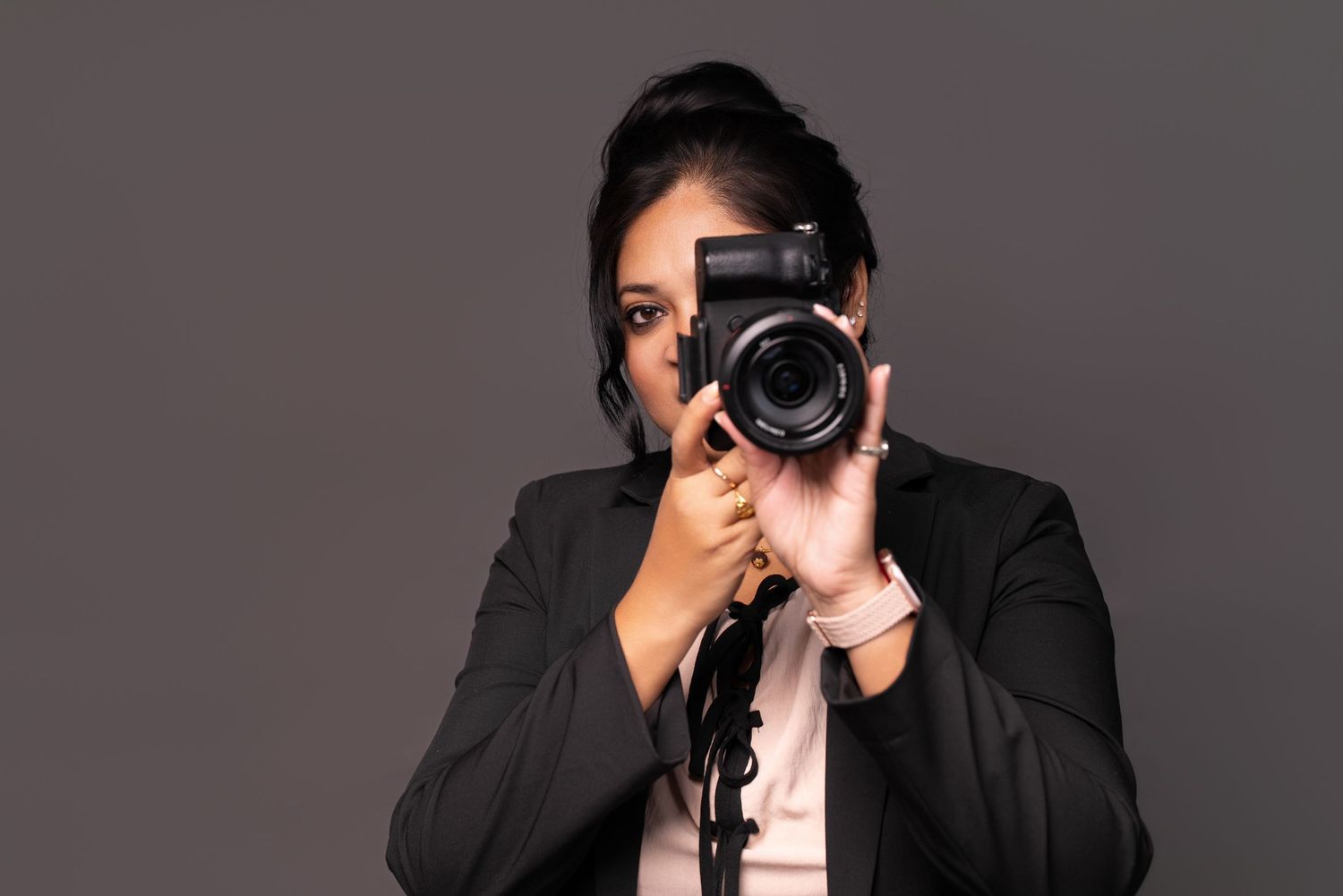 Professional photographer wearing black suit holds DSLR camera while taking photos in studio setting.