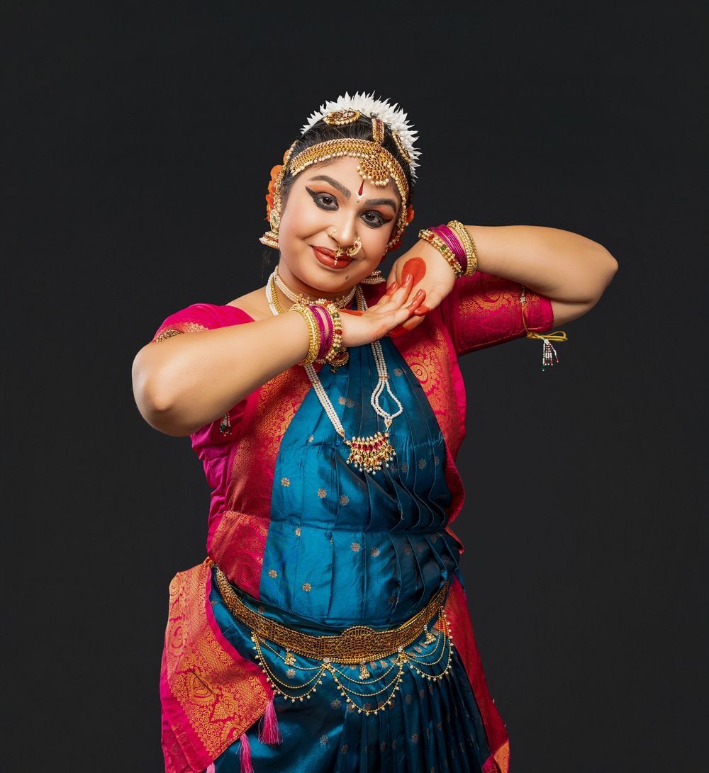 A dancer in traditional Indian attire performs expressive hand gestures in a classical dance pose against a dark background.