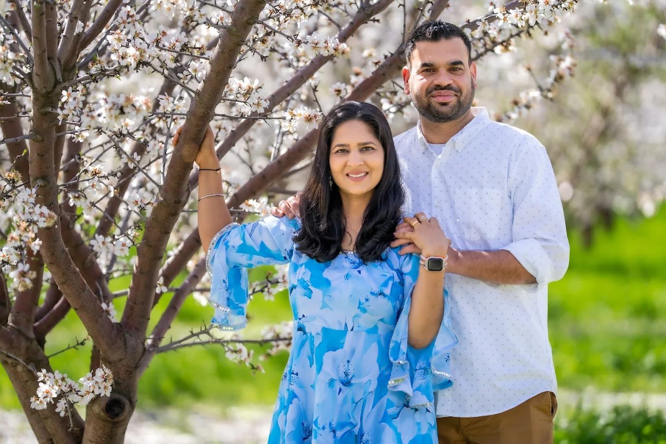 A couple poses together under blooming cherry blossom trees during a spring photo session.