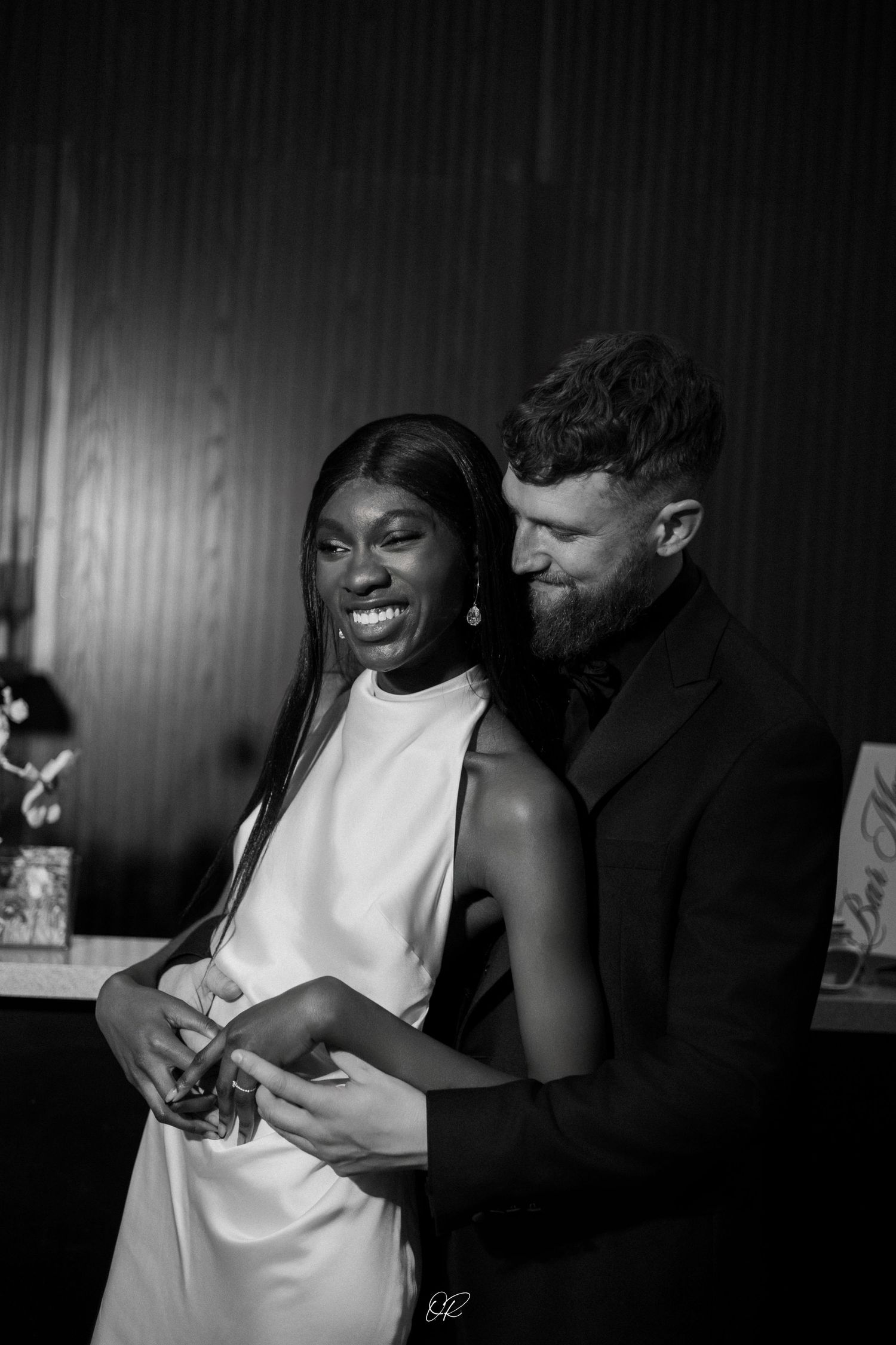 A black and white photo of a joyful couple embracing, with candid expressions captured in an intimate moment.