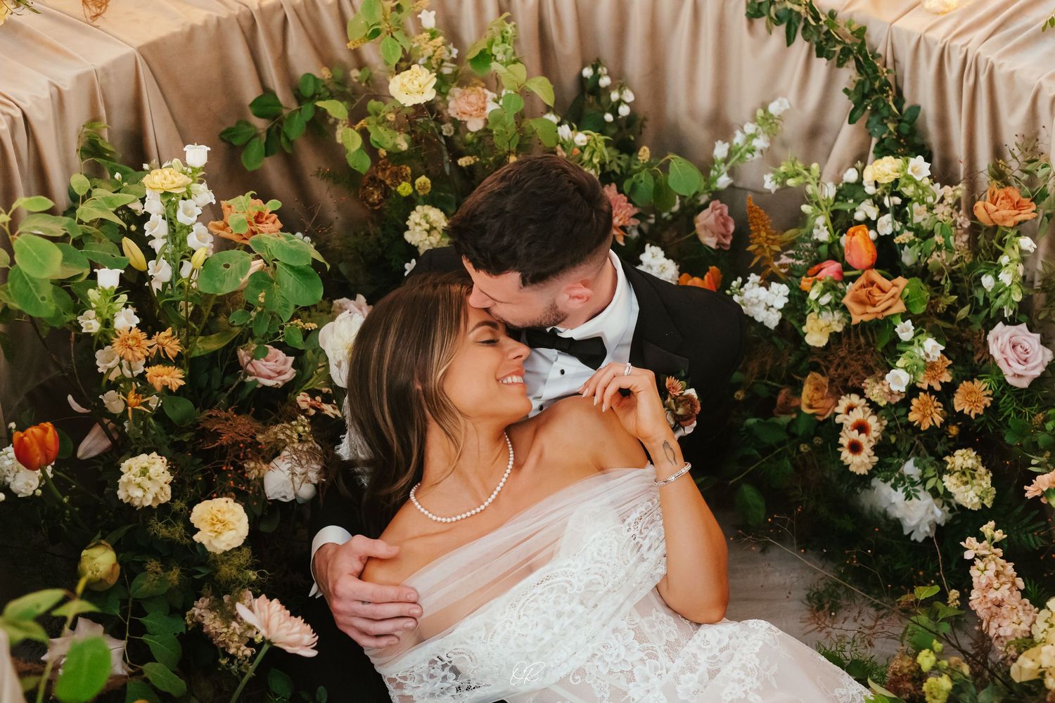 Romantic wedding scene surrounded by lush floral arrangements featuring peach and blush roses and greenery.