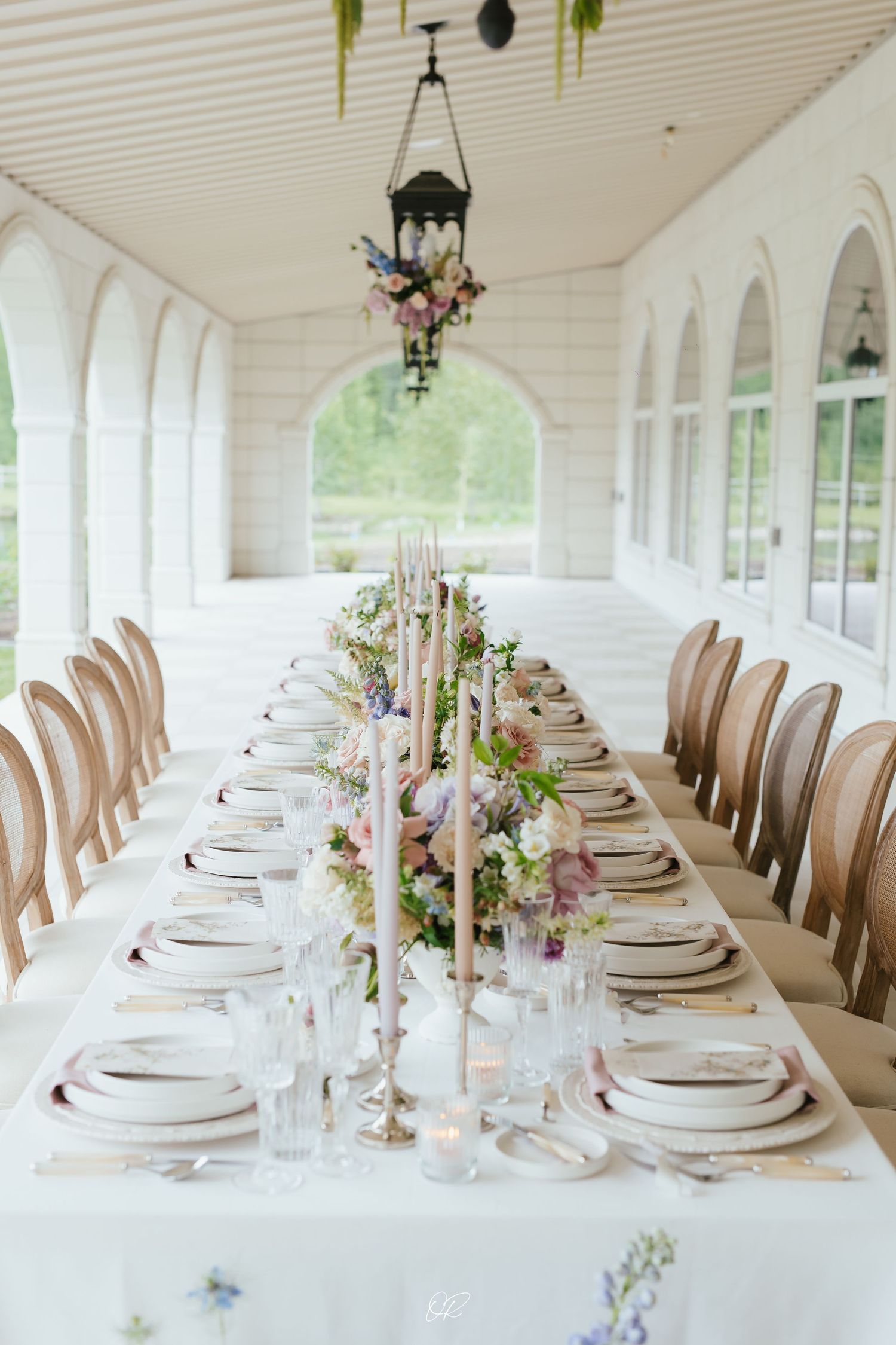 Elegant white porch table setting with pink floral centerpieces and tapered candles along a long formal dining arrangement.