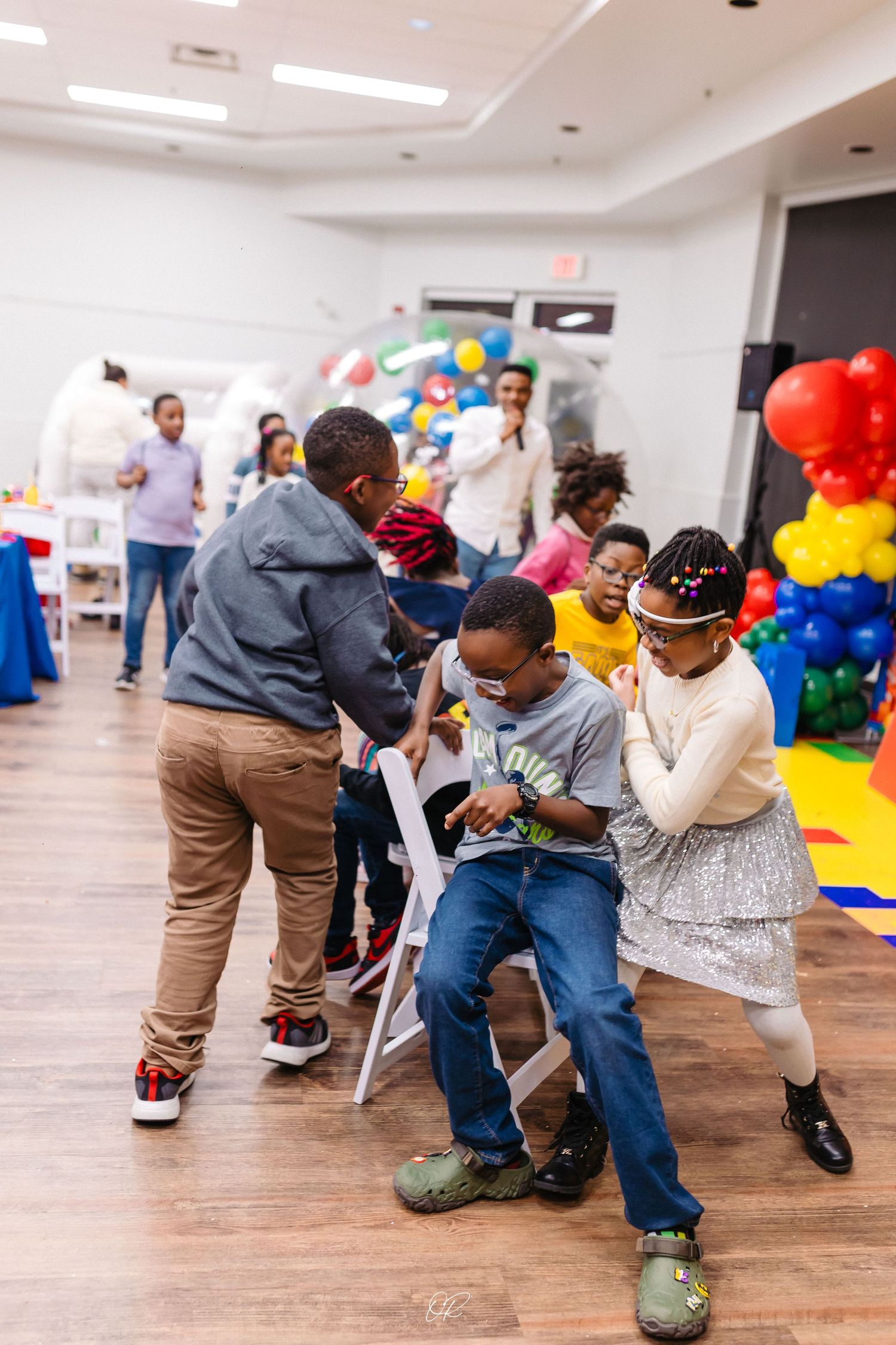 Children dance and play together at a festive party decorated with colorful balloon arrangements on a wooden floor.