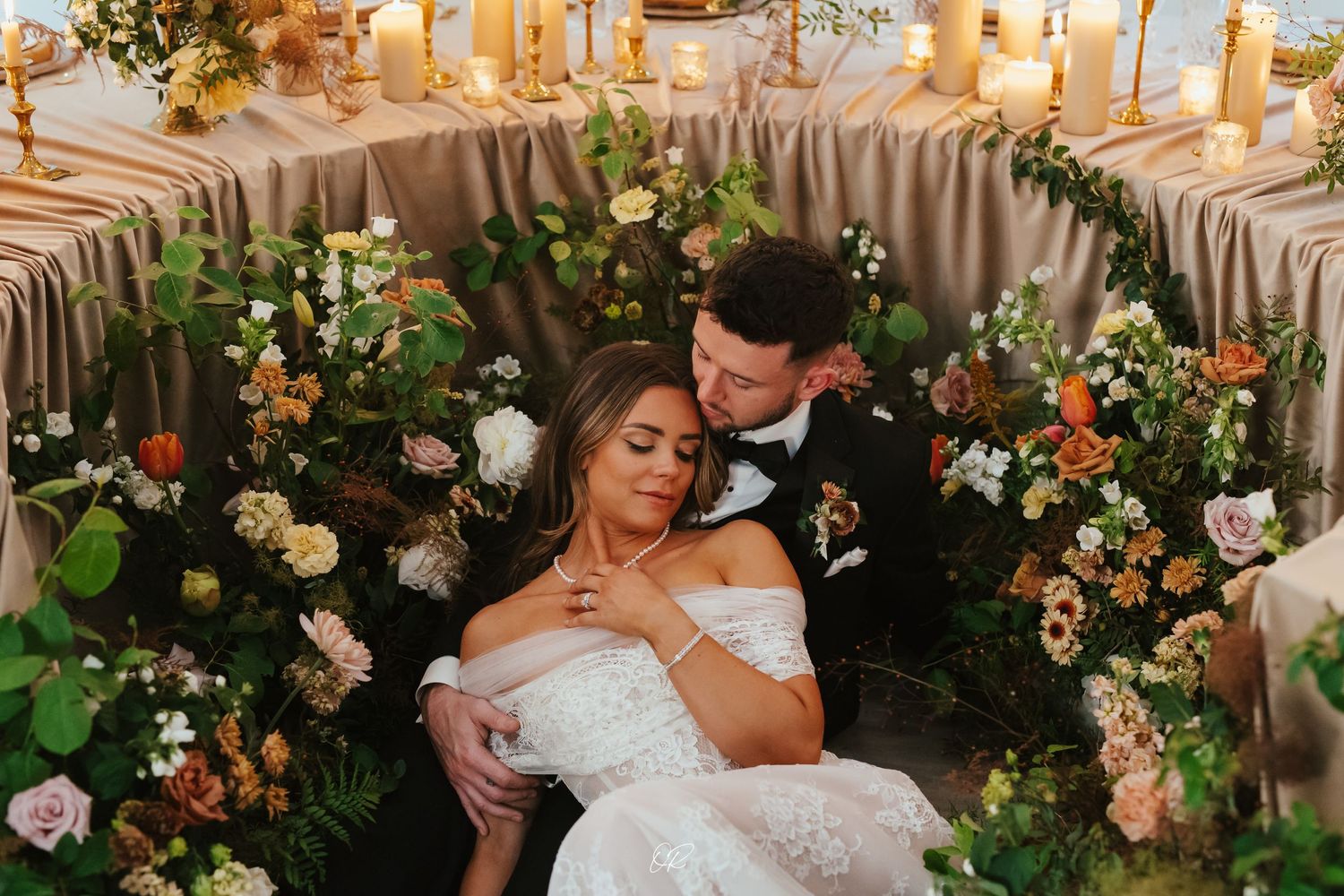 A romantic couple embraces in front of an elegant floral arch with peach and cream roses at a wedding reception.