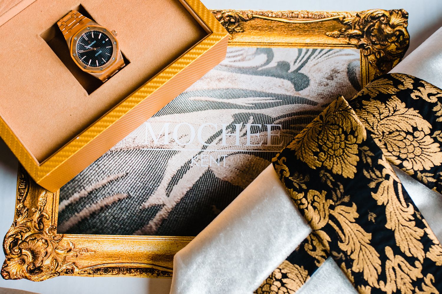 Vintage watch and ornate gold frame displayed with decorative items on peach surface.