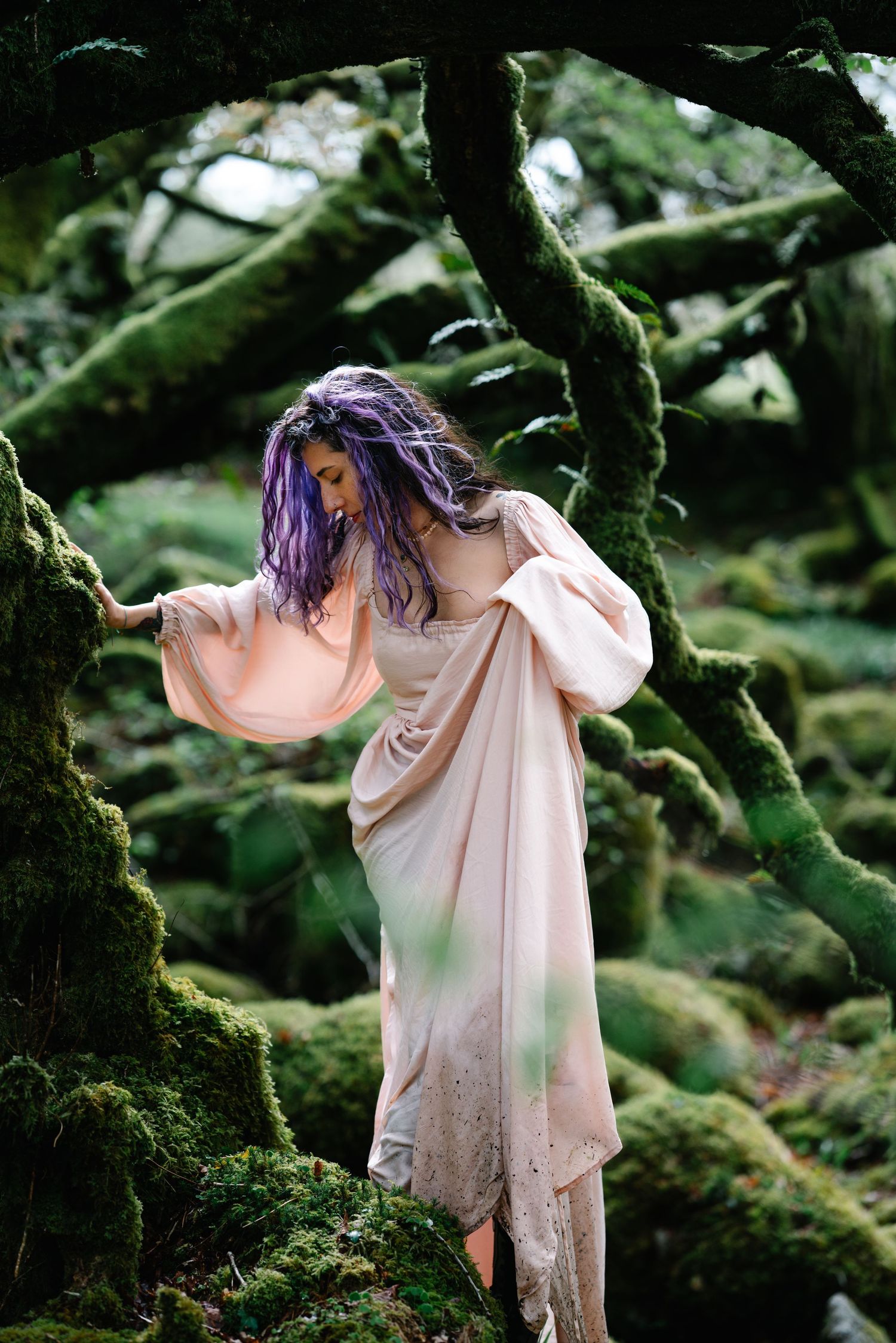 A person in a flowing pink dress moves gracefully among mossy trees in an enchanted forest setting.