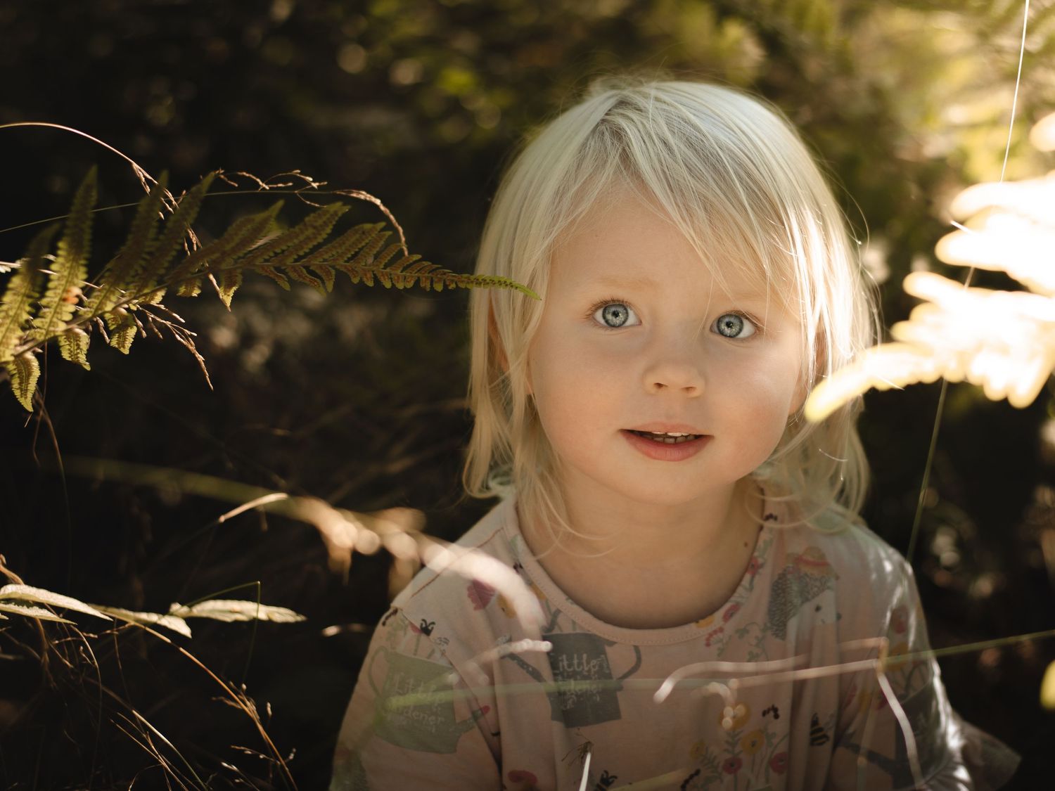 barn tittar mot kameran sittandes i lummig sörmländsk skog vid barnfotografering
