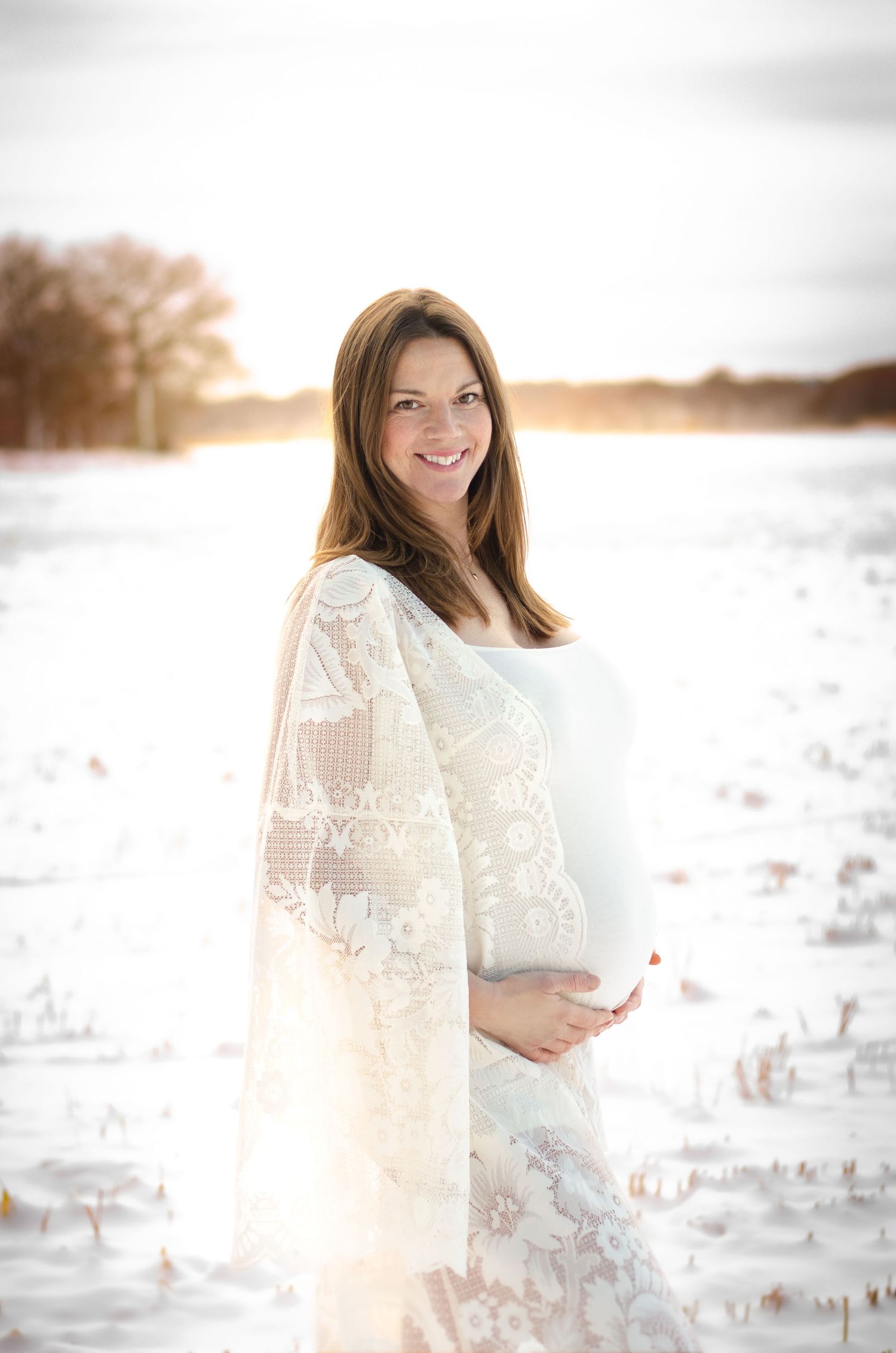 gravid kvinna i bohemisk spetskimono ler i solnedgången vid gravidfotografering i stockholm