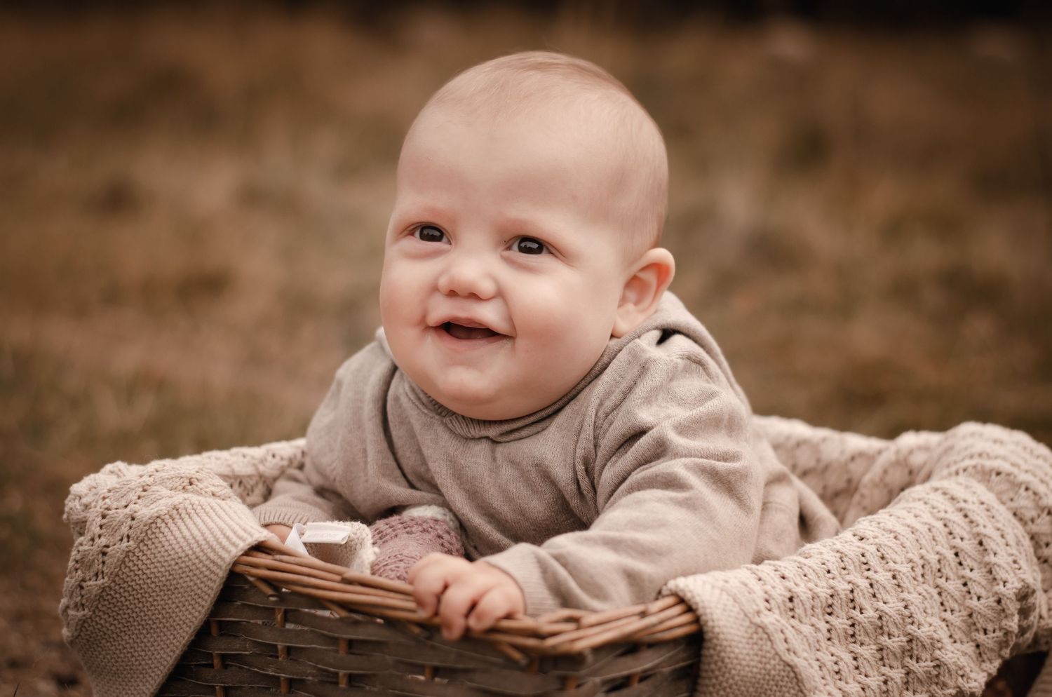 småbarn sitter i korg med filt och skrattar åt något som mamma gör bakom fotografen under barnfotografering i nyköping