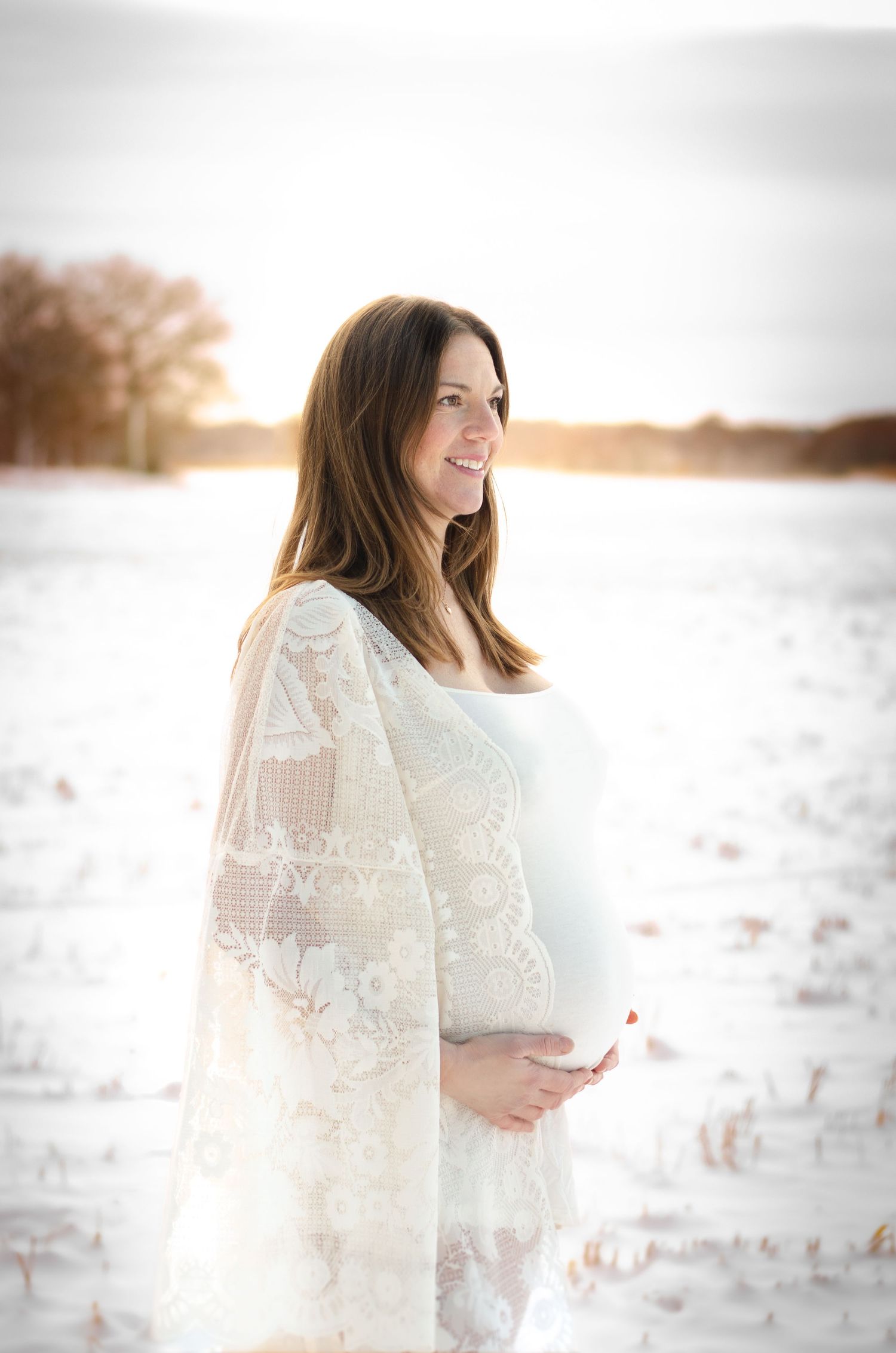 gravid kvinna i bohemisk kimono ler i solnedgången vid gravidfotografering i stallarholmen