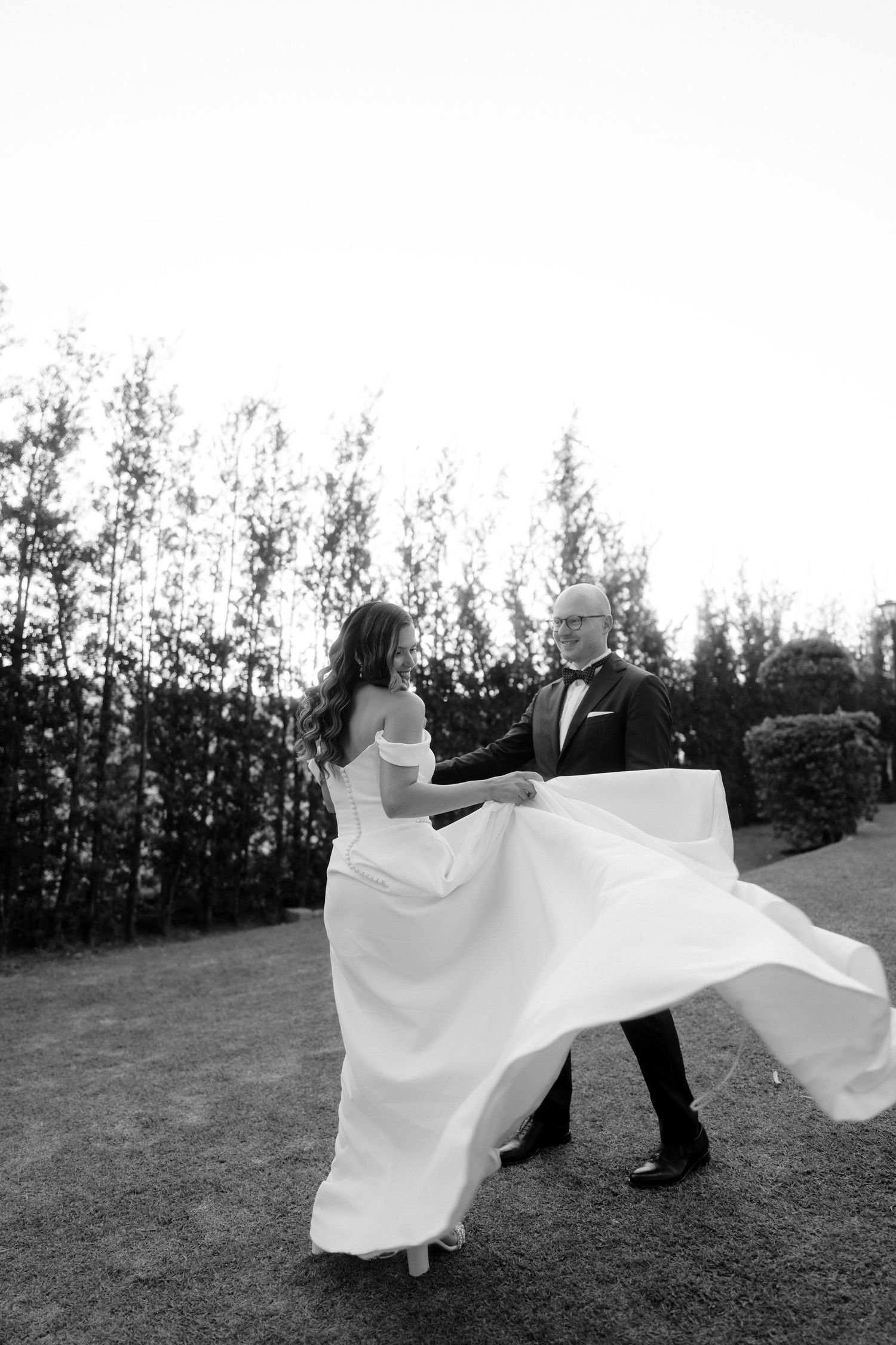 A couple dances gracefully in a field with flowing white fabric creating elegant movement in black and white photography.