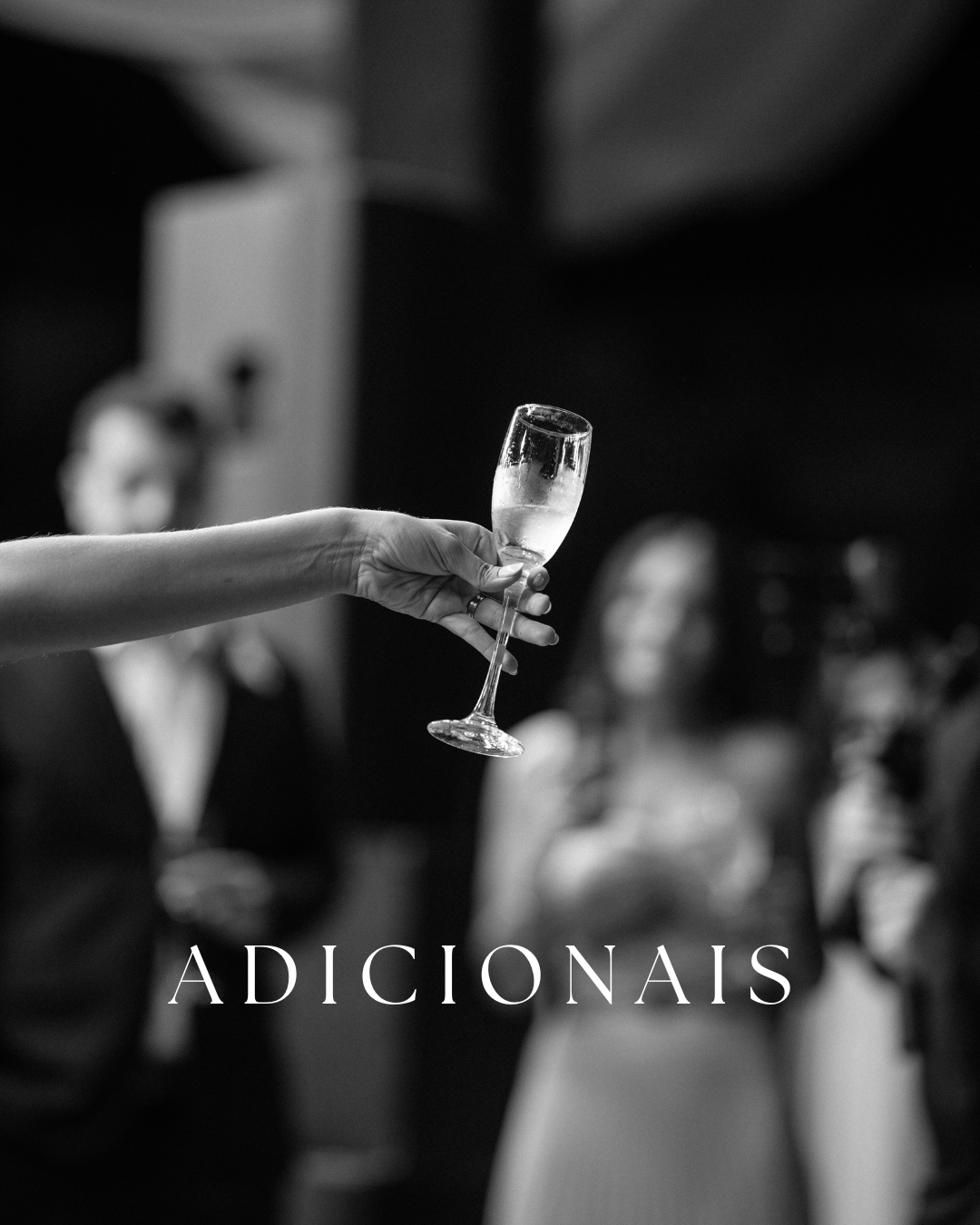 Blurred black and white image shows silhouettes of wine glasses and people in an elegant dining setting.