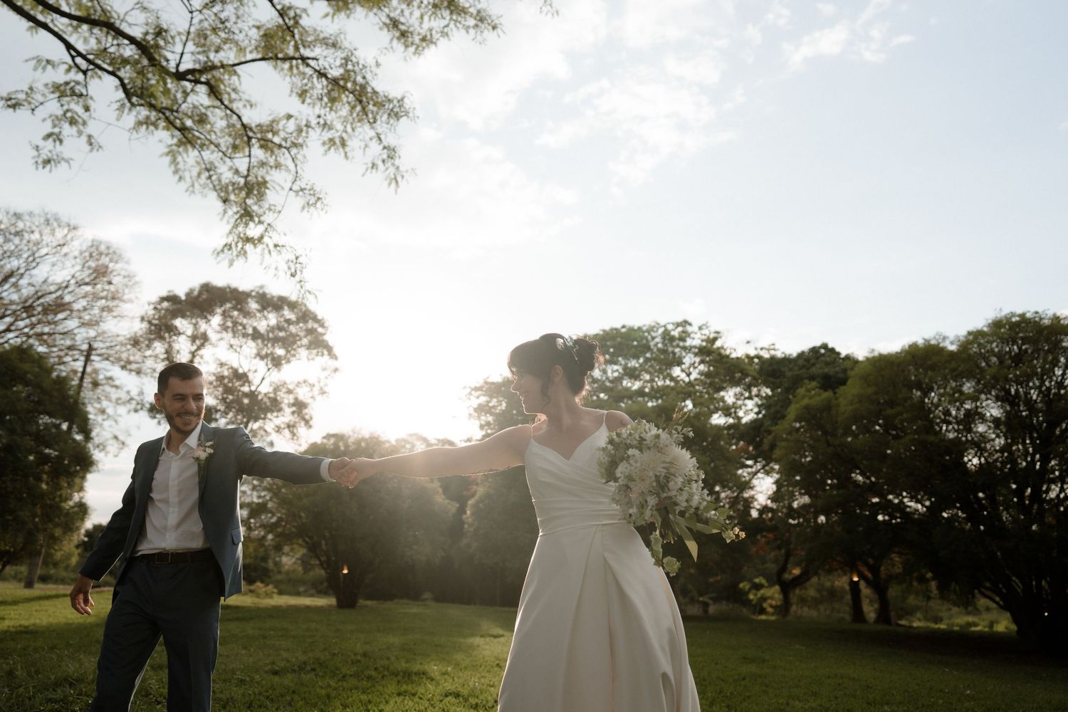 Newlyweds share a romantic moment in a sunlit garden during golden hour as trees create a dreamy backdrop.