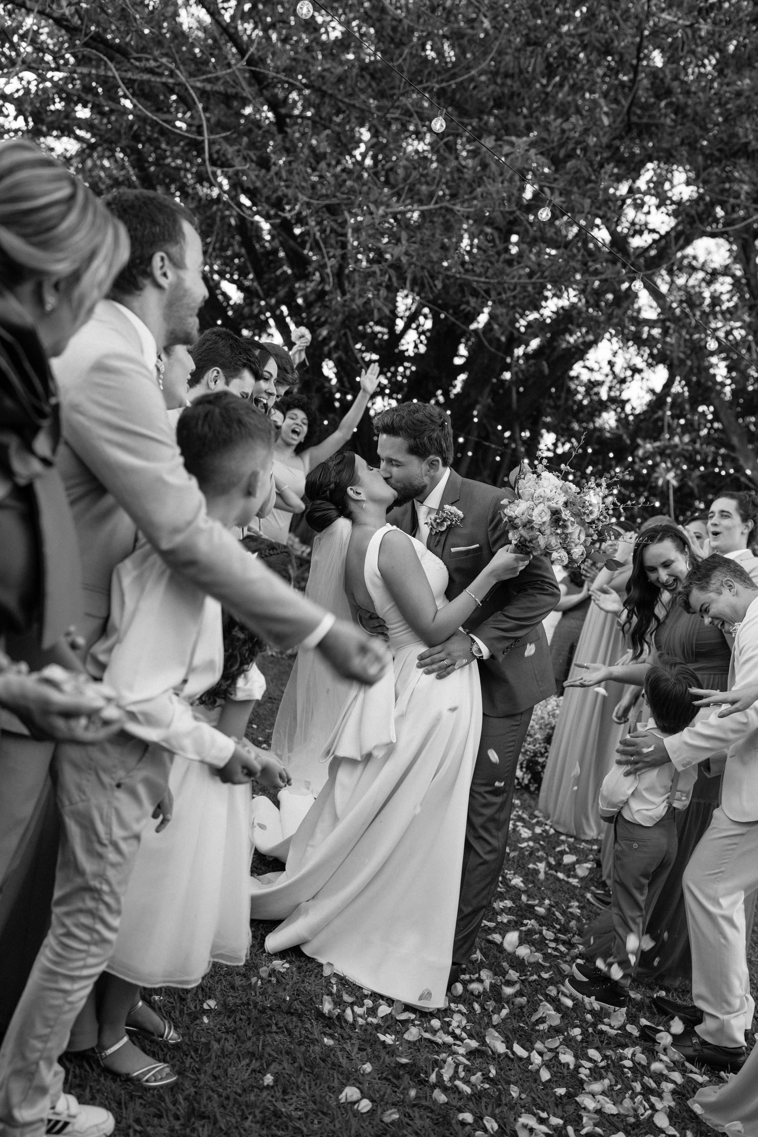 A black and white photo series showing a group dancing and celebrating together outdoors under trees.