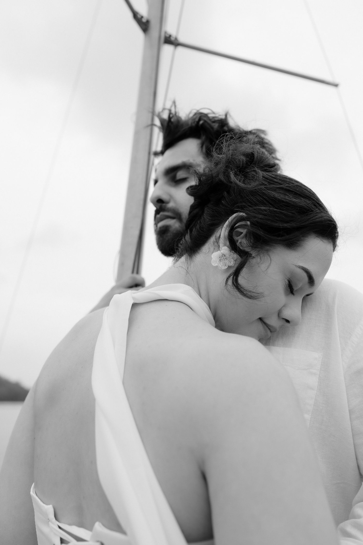 Black and white romantic portrait of a couple embracing back to back on a sailboat.