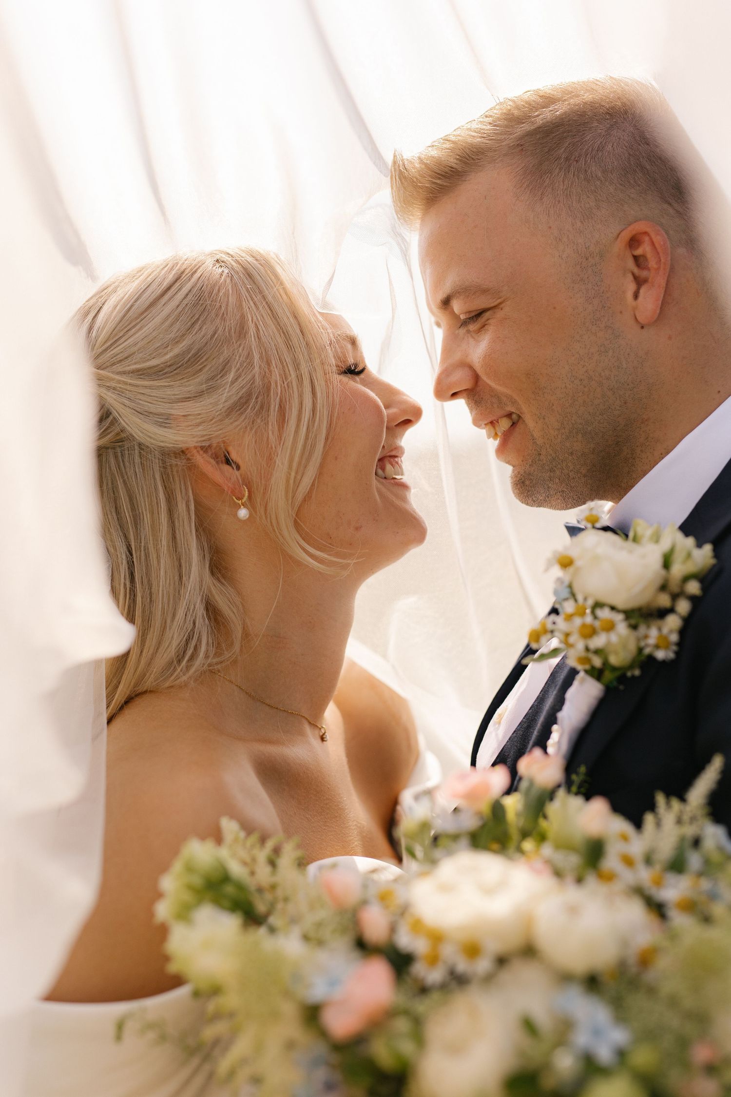 Joyful couple shares intimate moment on their wedding day with soft lighting and floral bouquet details.