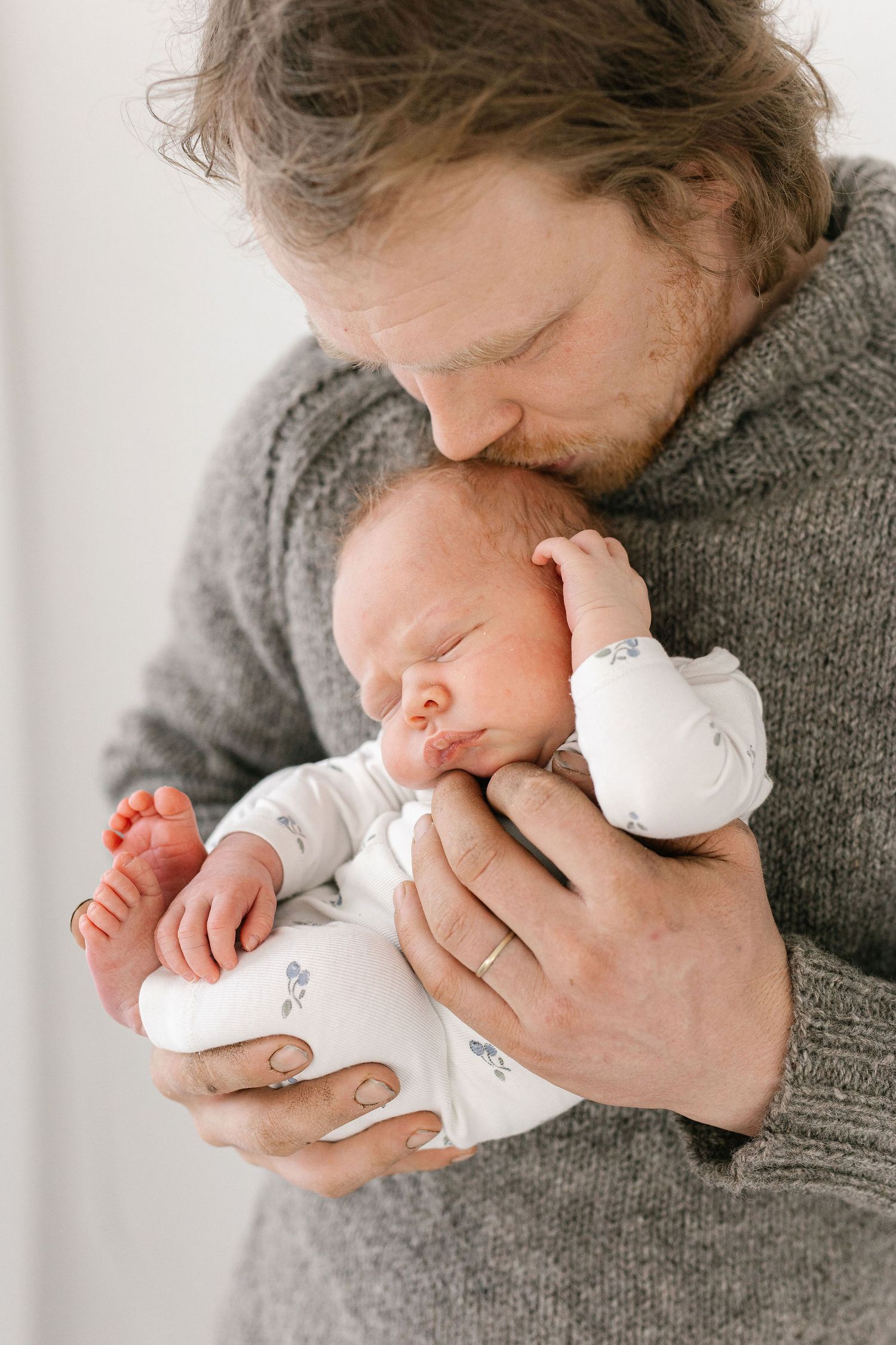 Parent in gray sweater holding sleeping newborn close to chest.