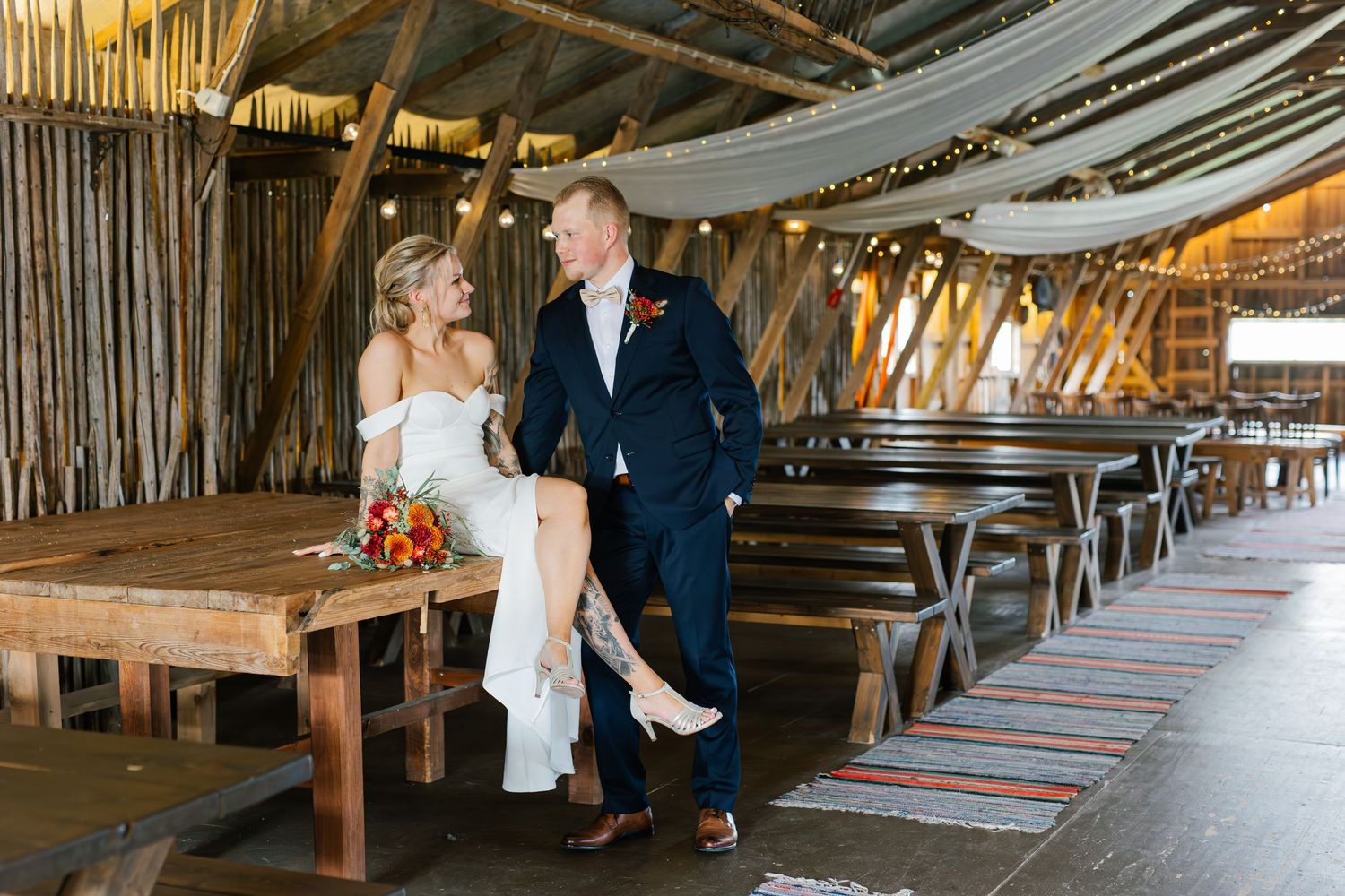 A rustic barn wedding venue interior with draped fabric and string lights creating a romantic ambiance.