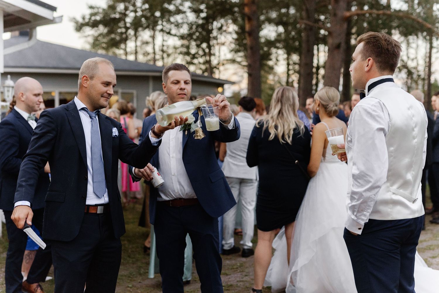 Wedding guests celebrating and toasting outdoors at a forest venue.