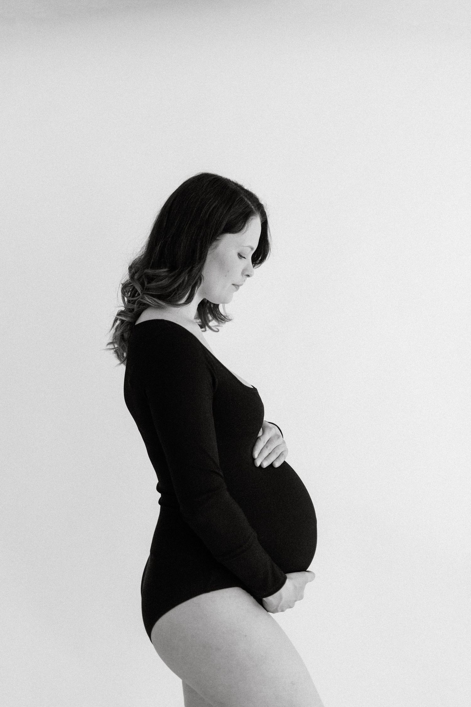 Side profile of pregnant woman in black bodysuit against white background.