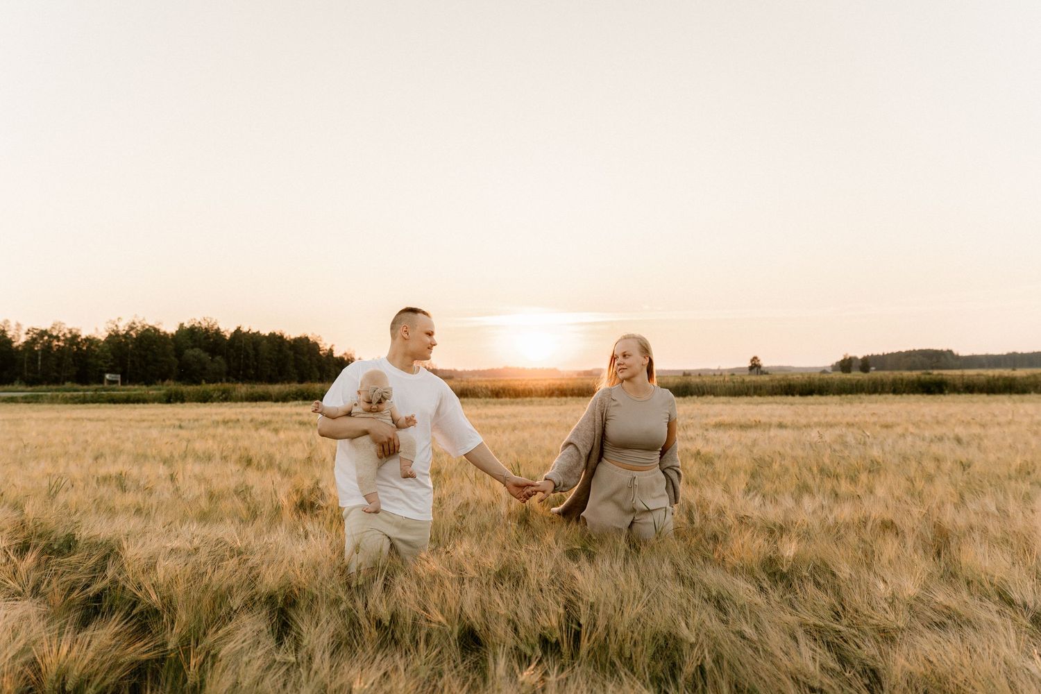 A couple holds hands while walking through a golden wheat field at sunset.