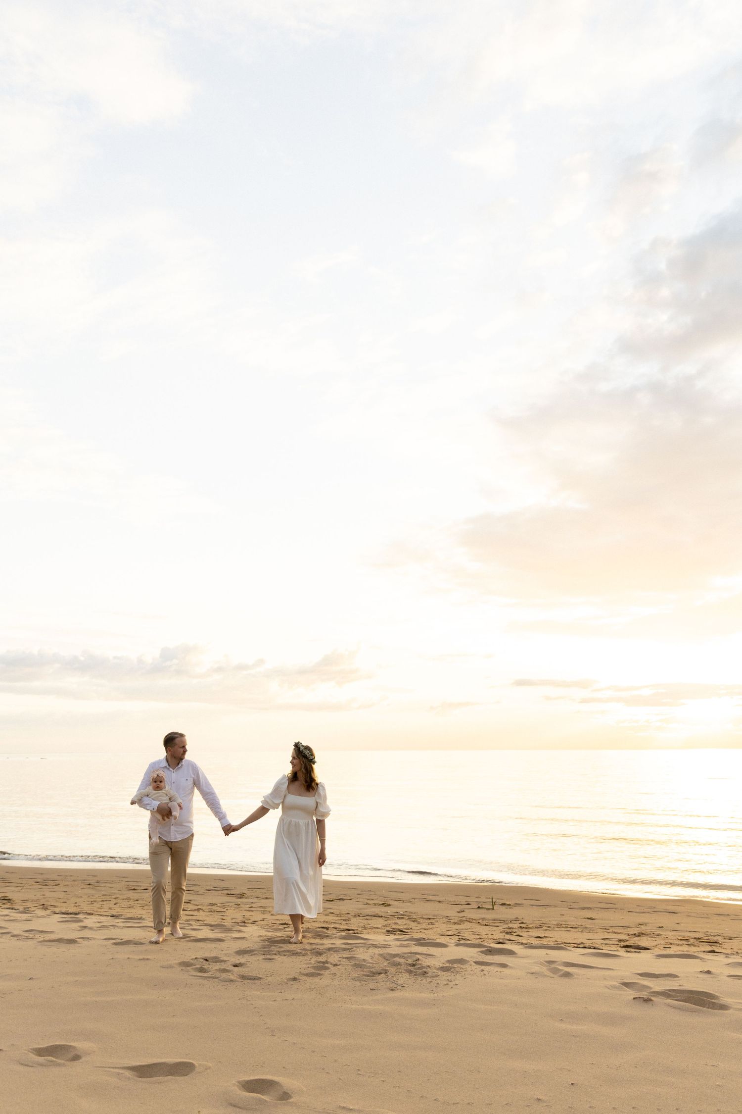 Couple walking hand in hand on beach at sunset wearing white outfits.