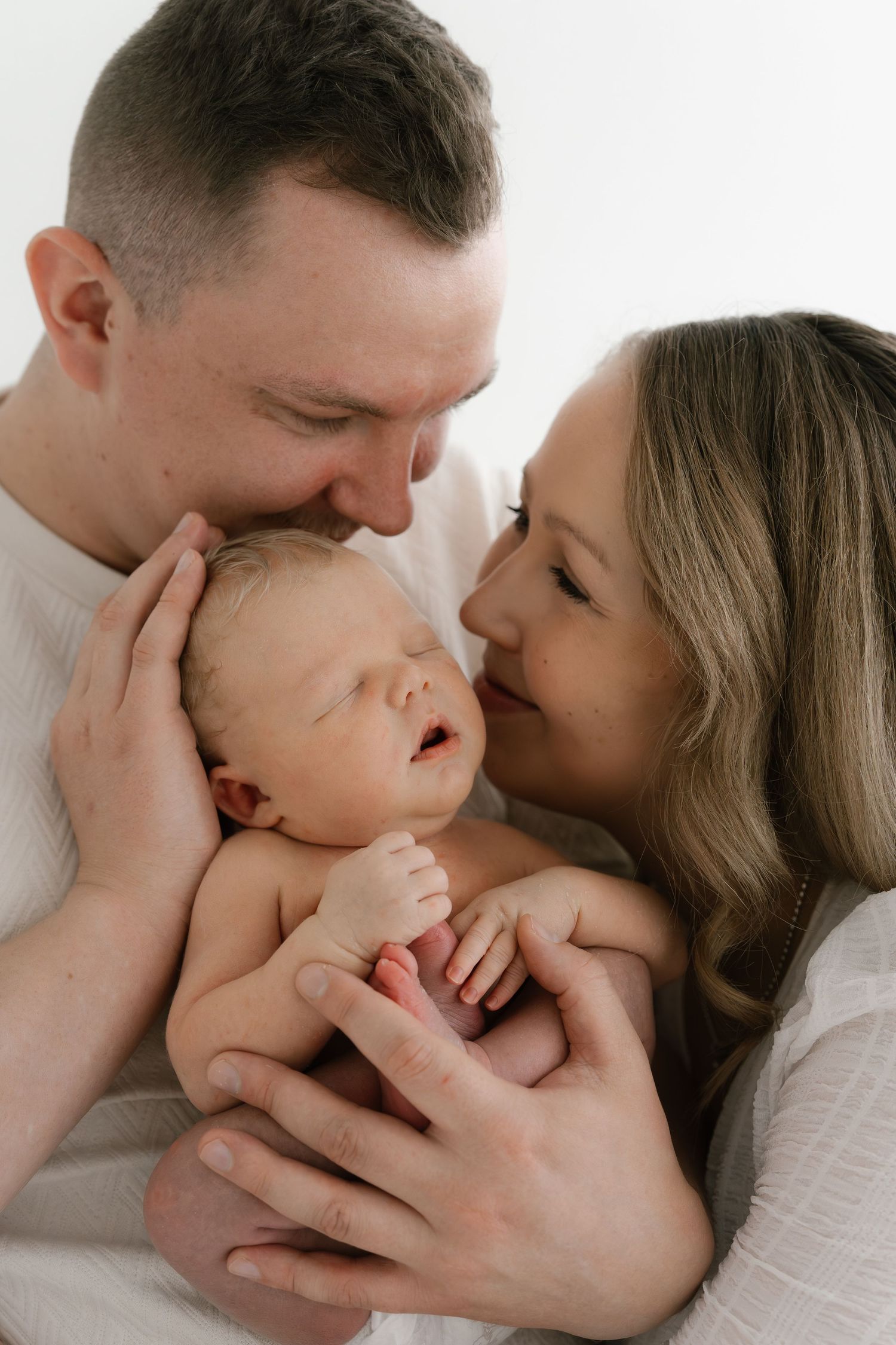 A couple tenderly holds their sleeping newborn baby close, sharing an intimate family portrait moment.