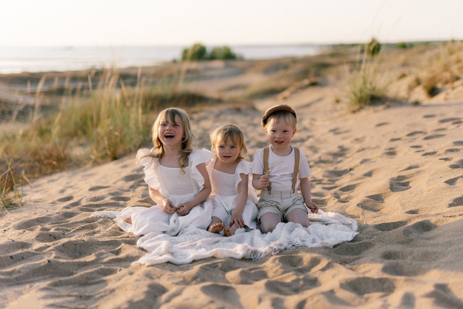 Three children sitting together on blanket at beach during golden hour.