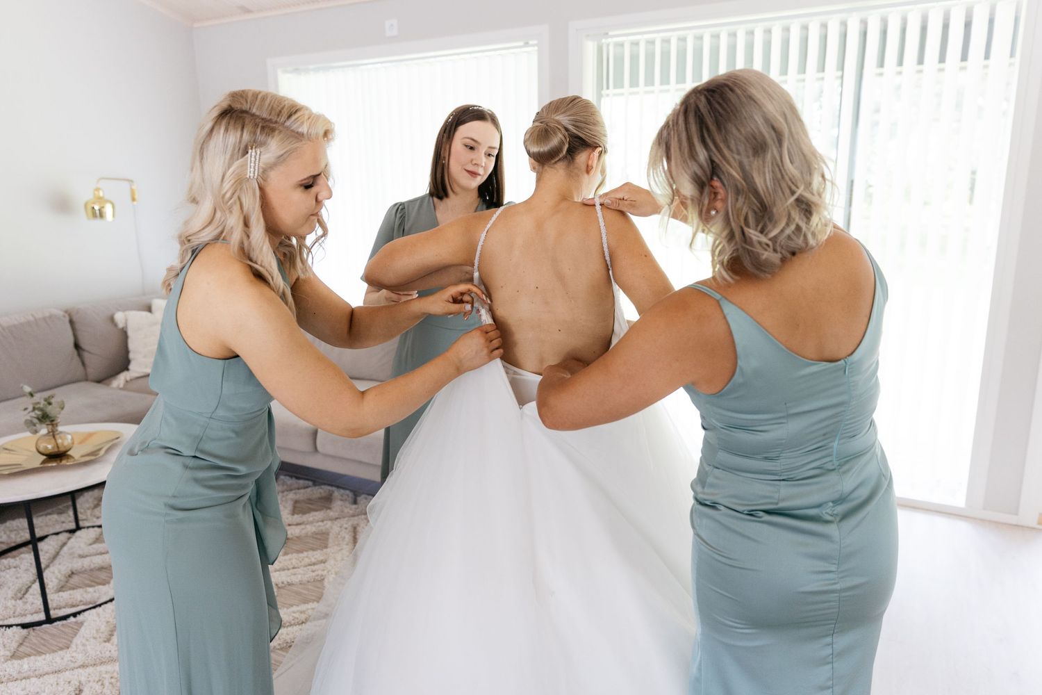 Bridesmaids in seafoam dresses helping with wedding dress preparations.
