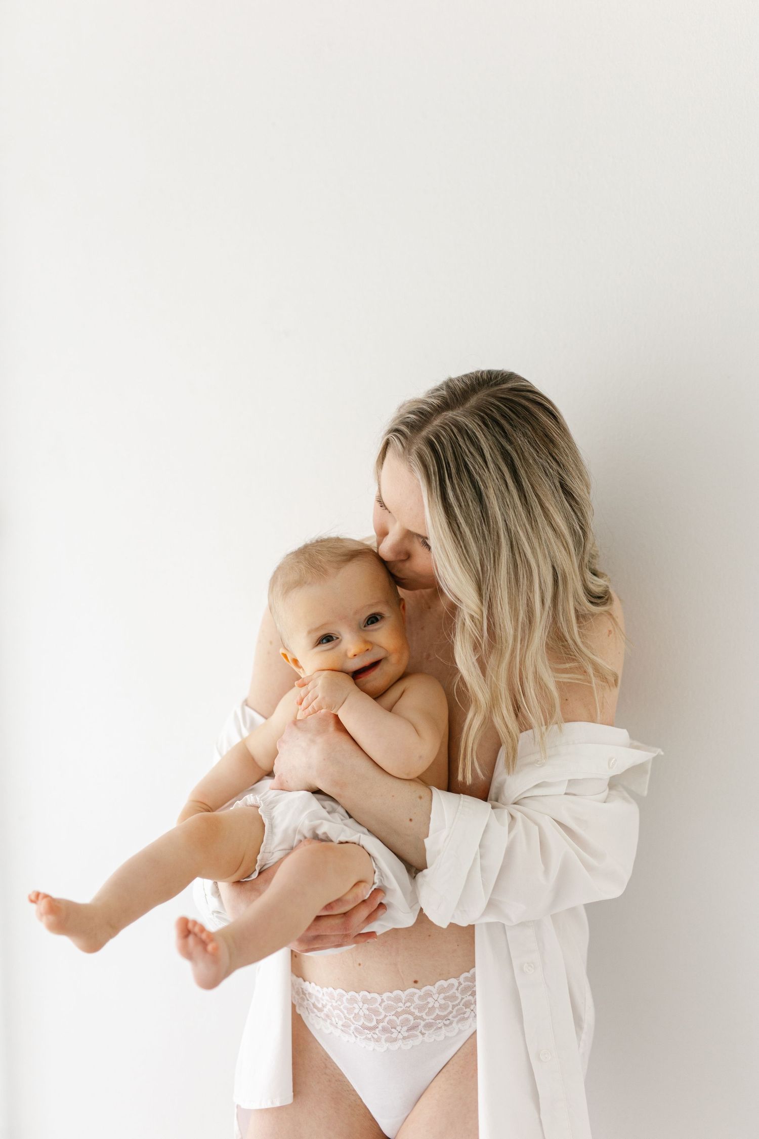 Candid mother and baby portrait in white against minimal background.