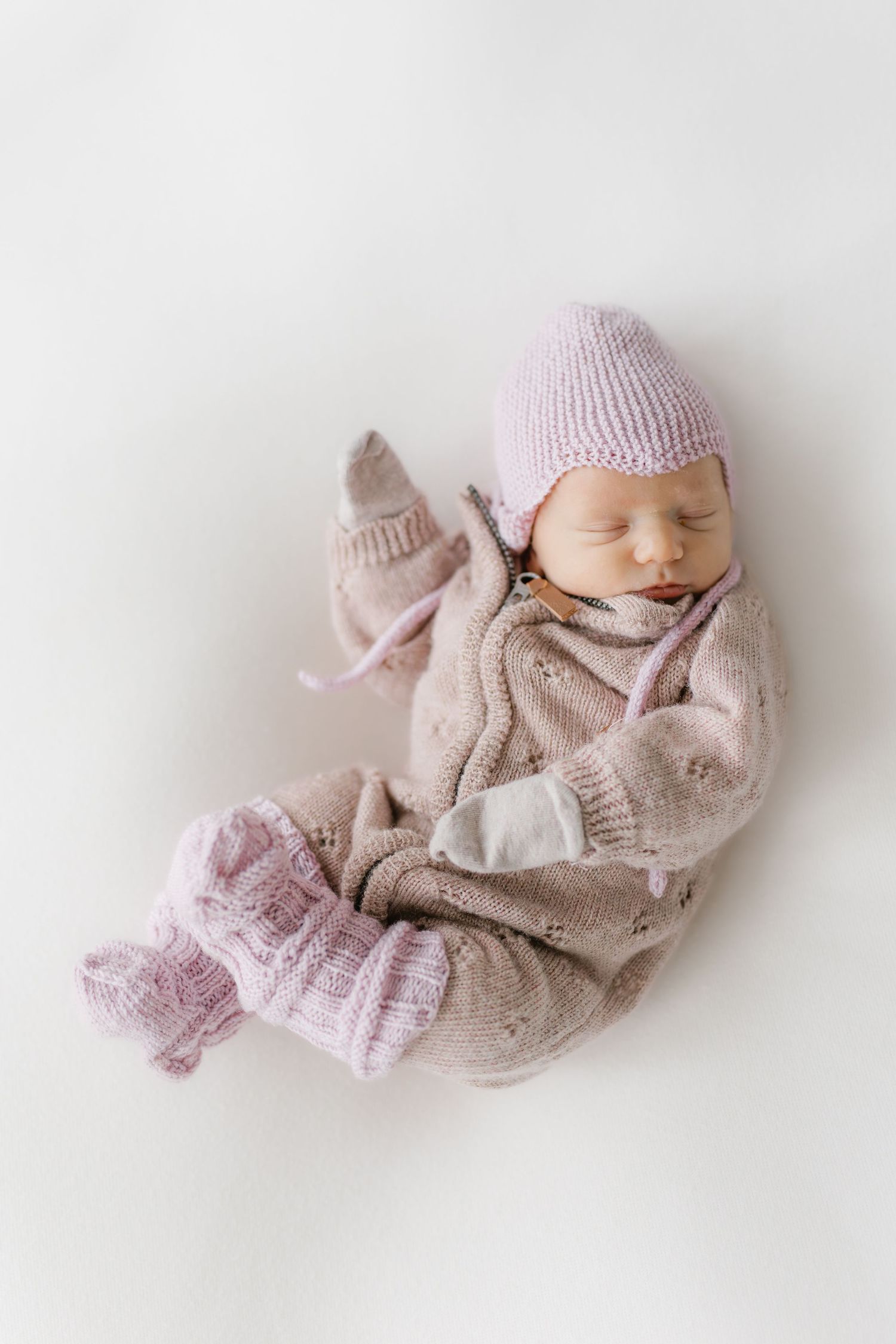 Sleeping newborn baby wearing soft pink knitted clothing and hat lies on white background in three poses.