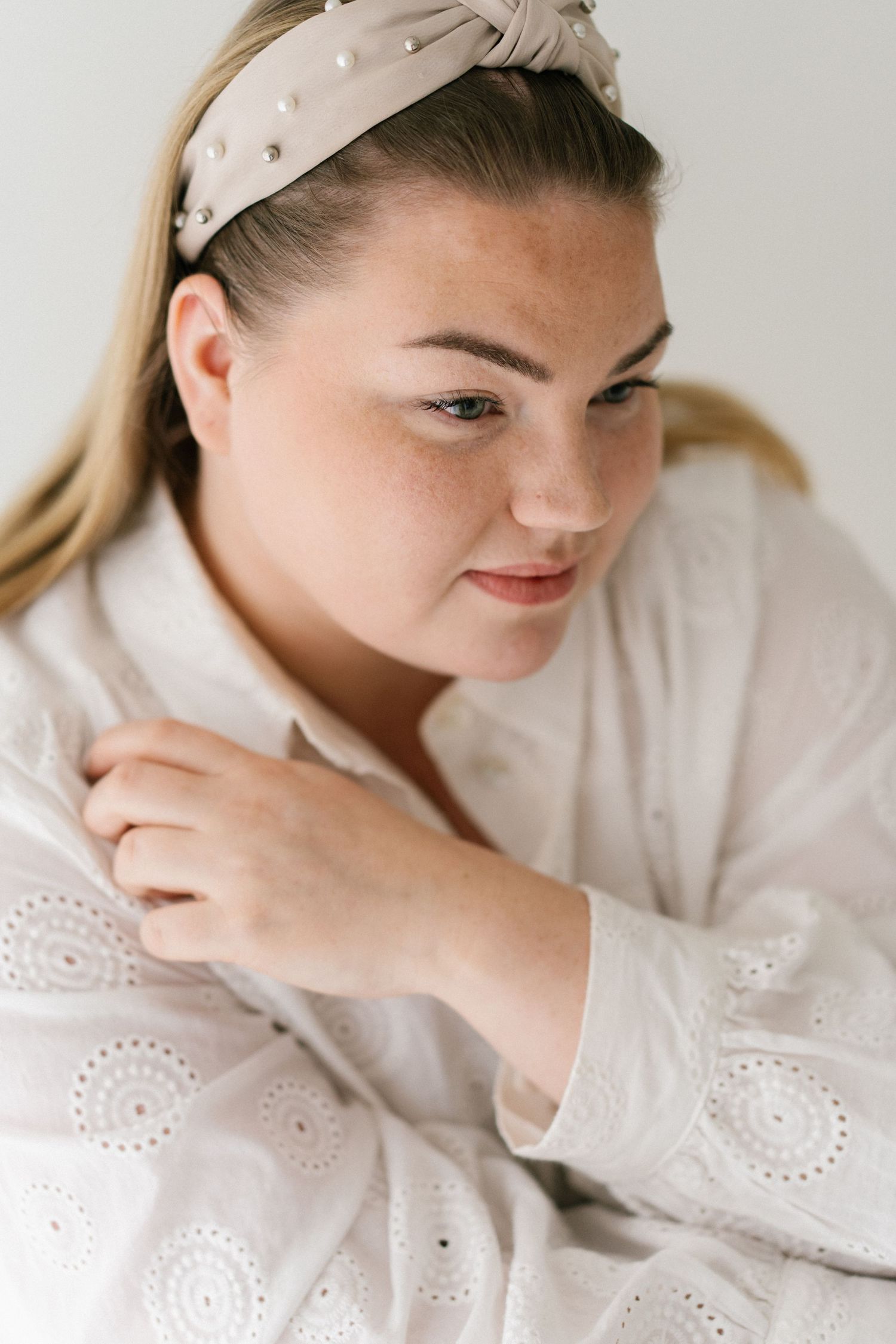 Person wearing polka dot headband and white eyelet dress poses against light background.