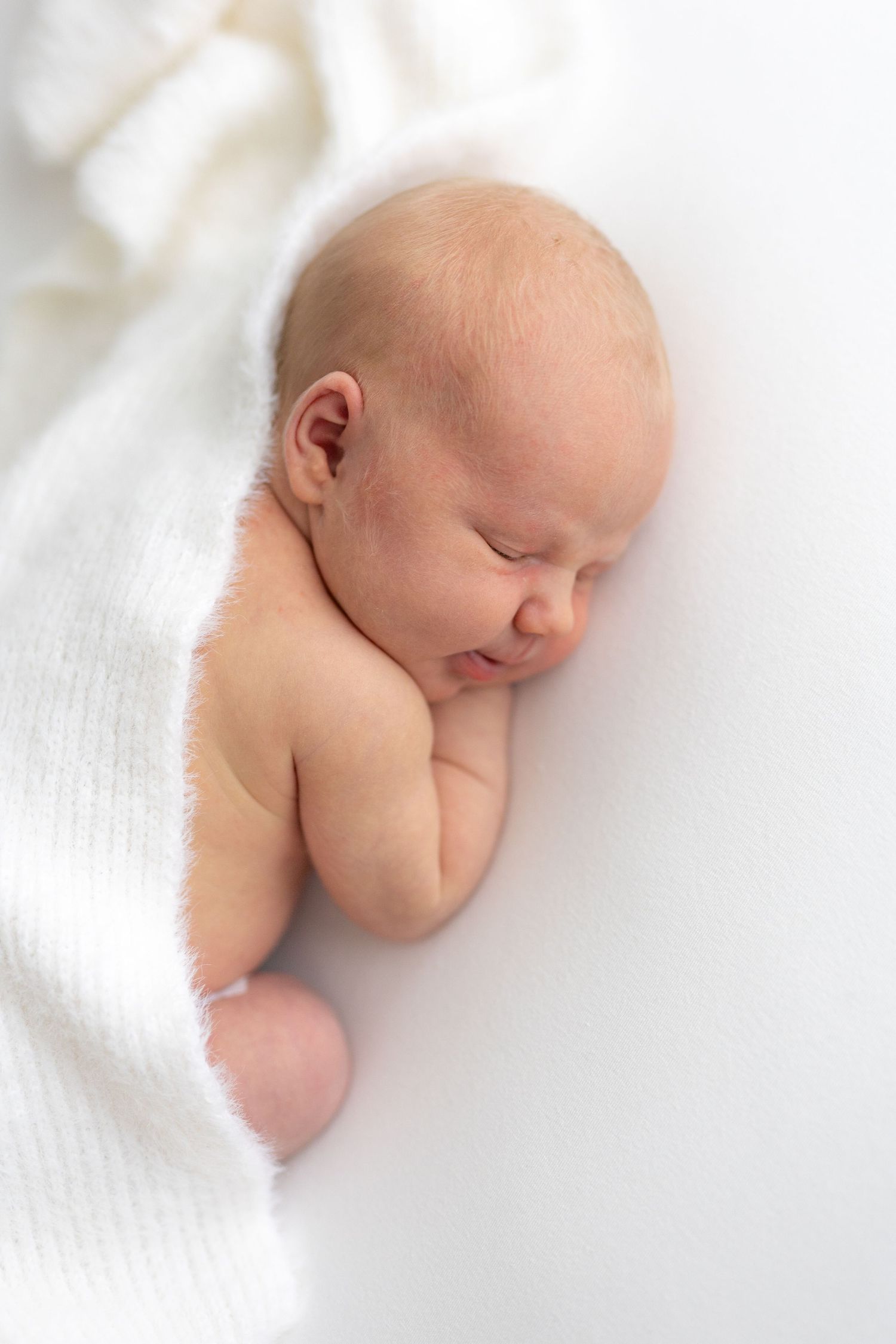 Sleeping newborn partially wrapped in white fabric against soft background.