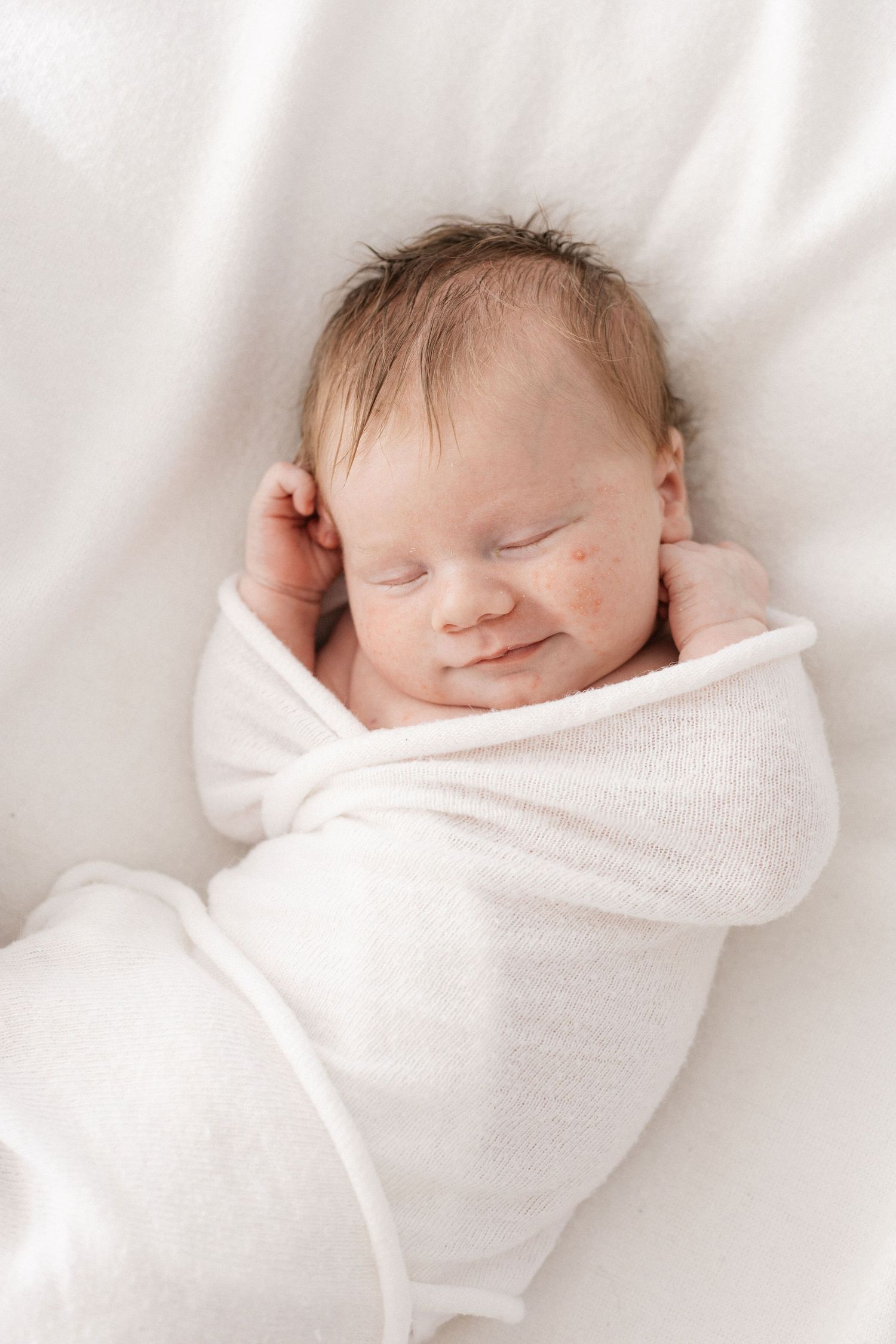 Peaceful sleeping newborn swaddled in white against soft textured background.