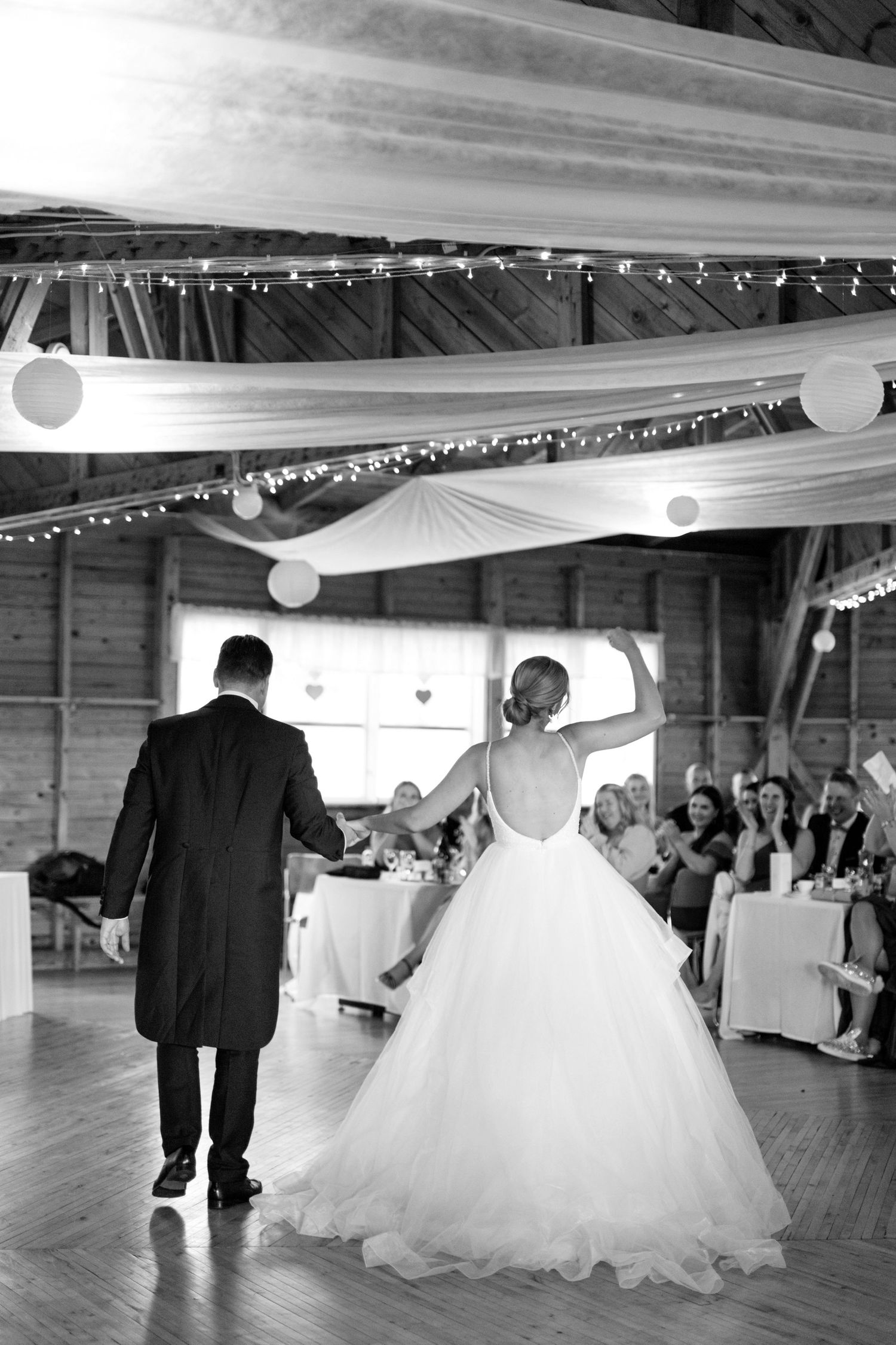 Black and white photo of couple's first dance in a rustic barn venue with twinkle lights.