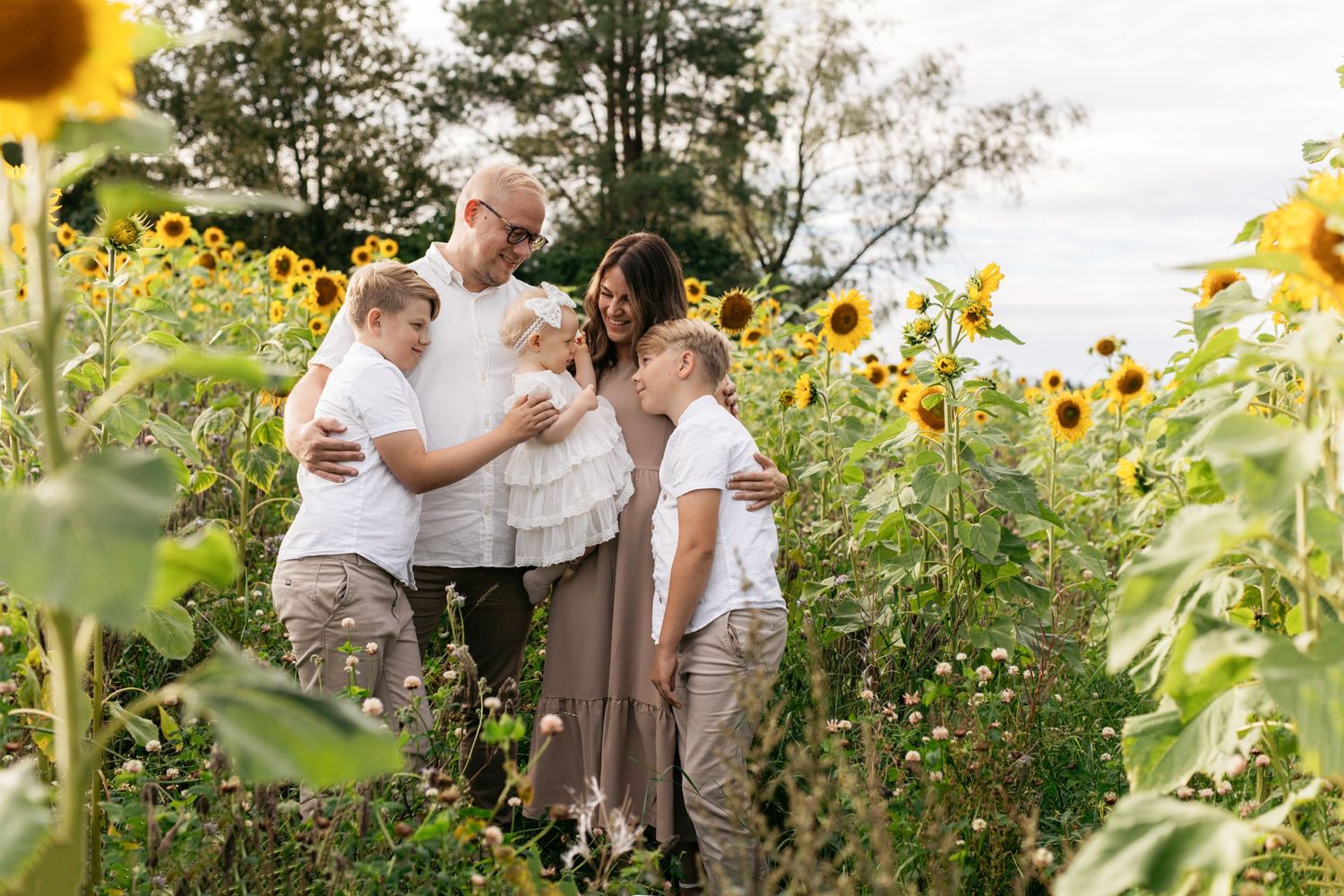 Family gathering among tall blooming sunflowers in a summer garden.