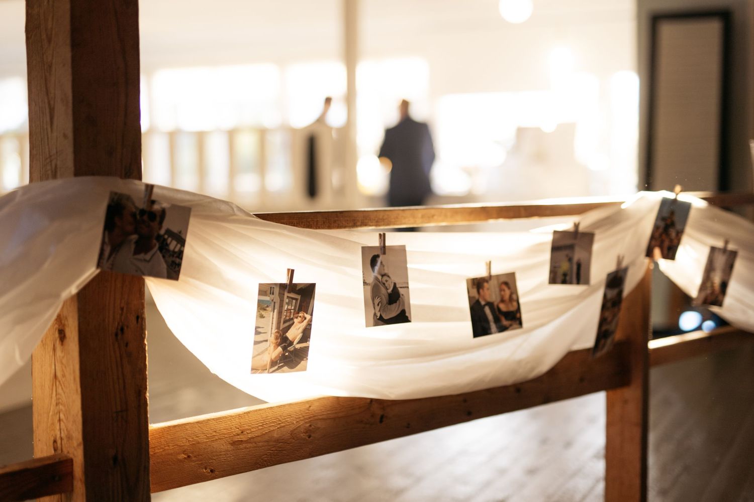 Vintage polaroid photographs hung on twine against white fabric and wooden beams in warm lighting.