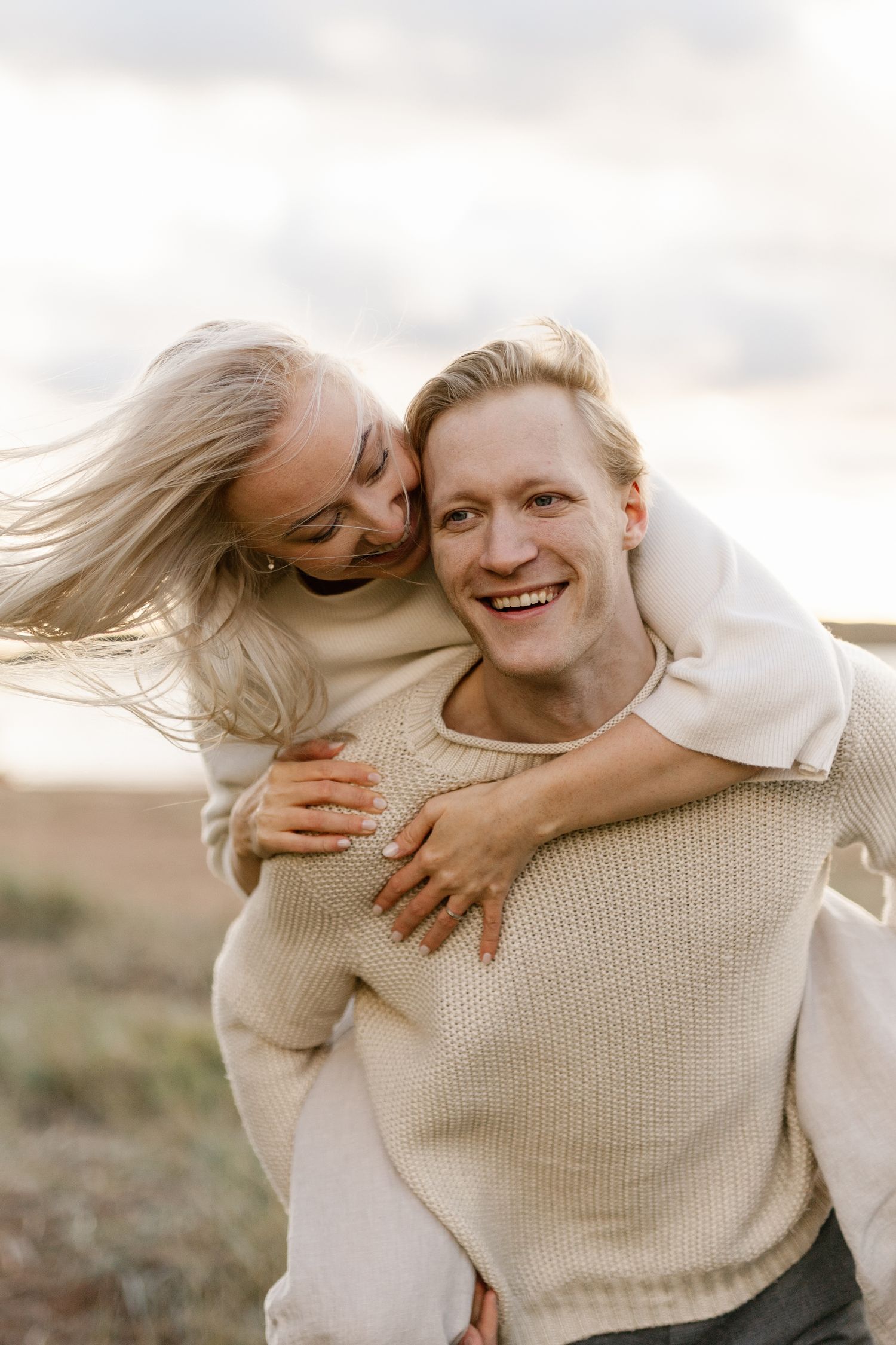 Happy couple sharing a joyful piggyback moment in casual sweaters during golden hour.