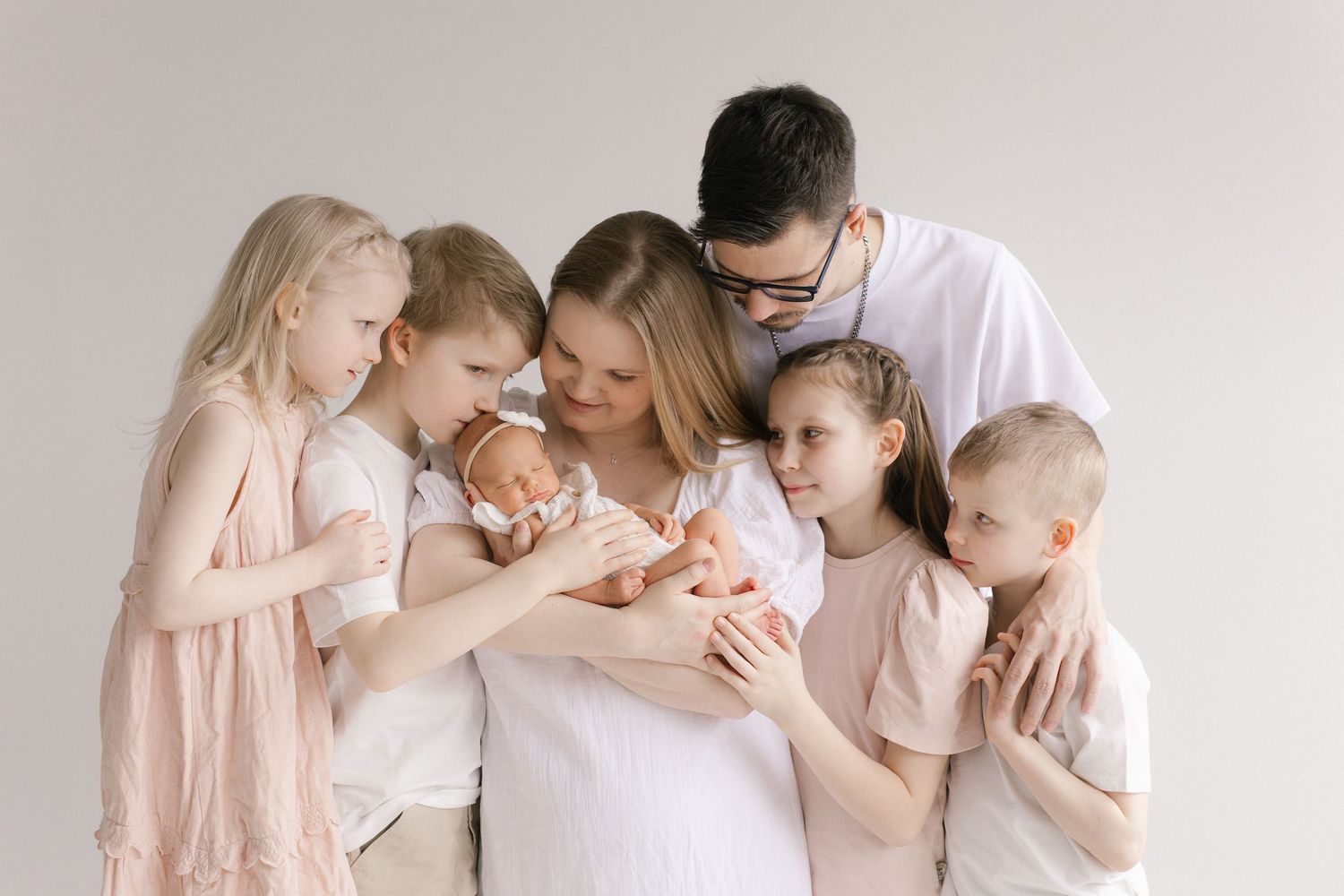 Family of seven with parents and five children, including a newborn baby, posing together in a bright studio portrait.