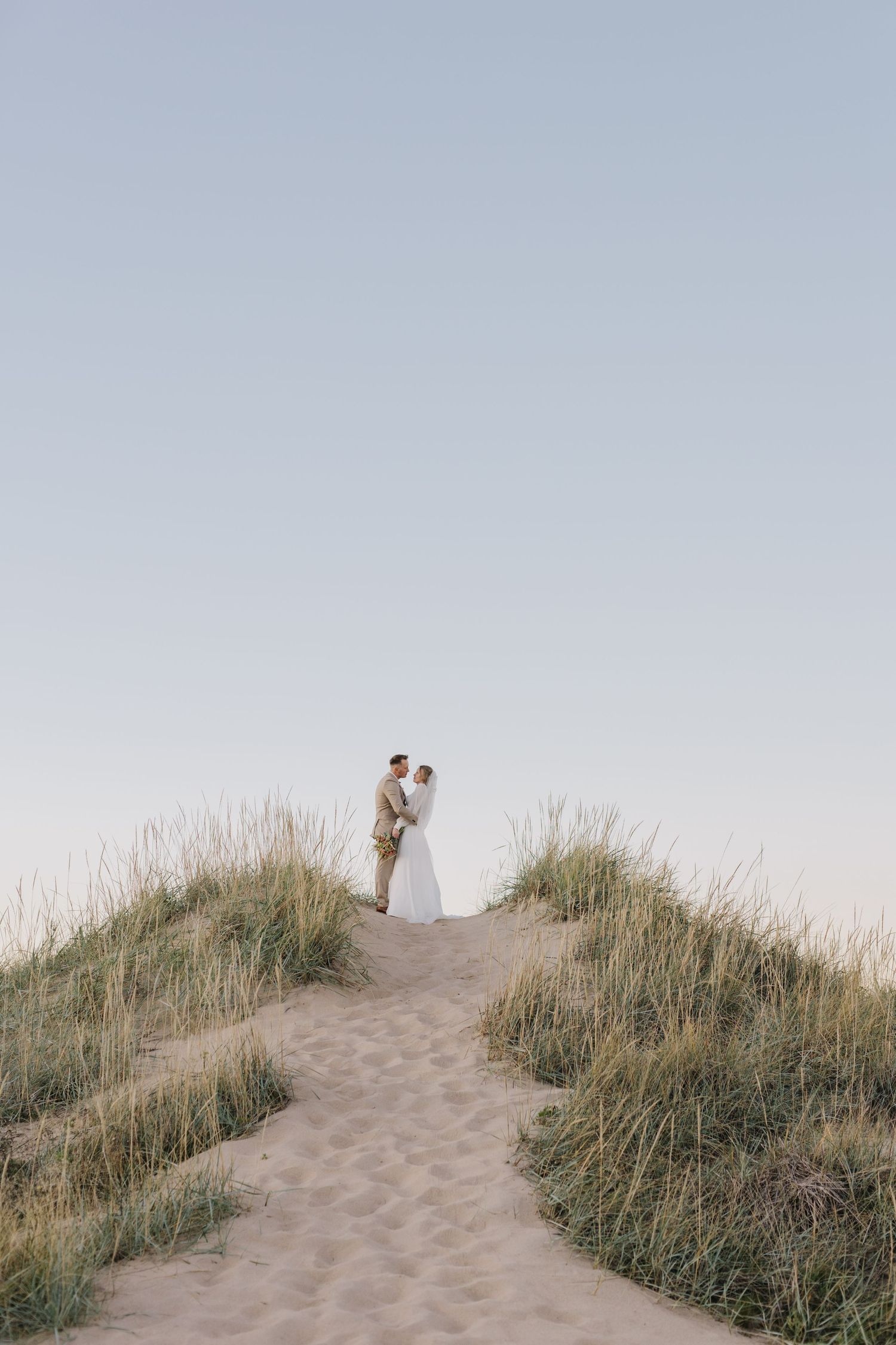 Romantic silhouette of couple standing on sandy hill against soft sky backdrop.