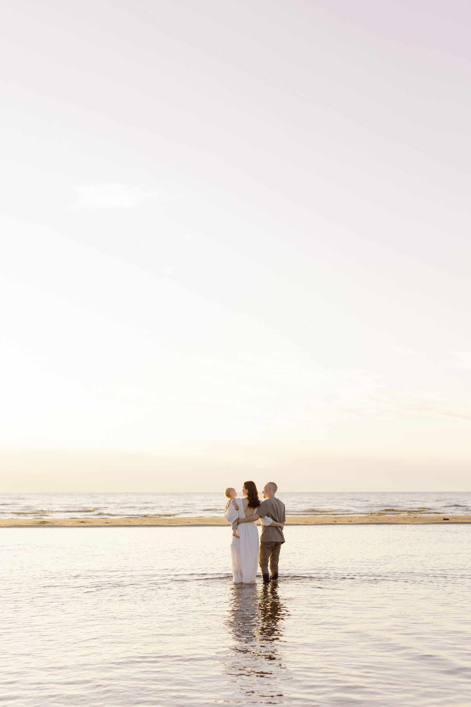 Three people walk along the shoreline at sunset, creating silhouettes against the golden water and sky.