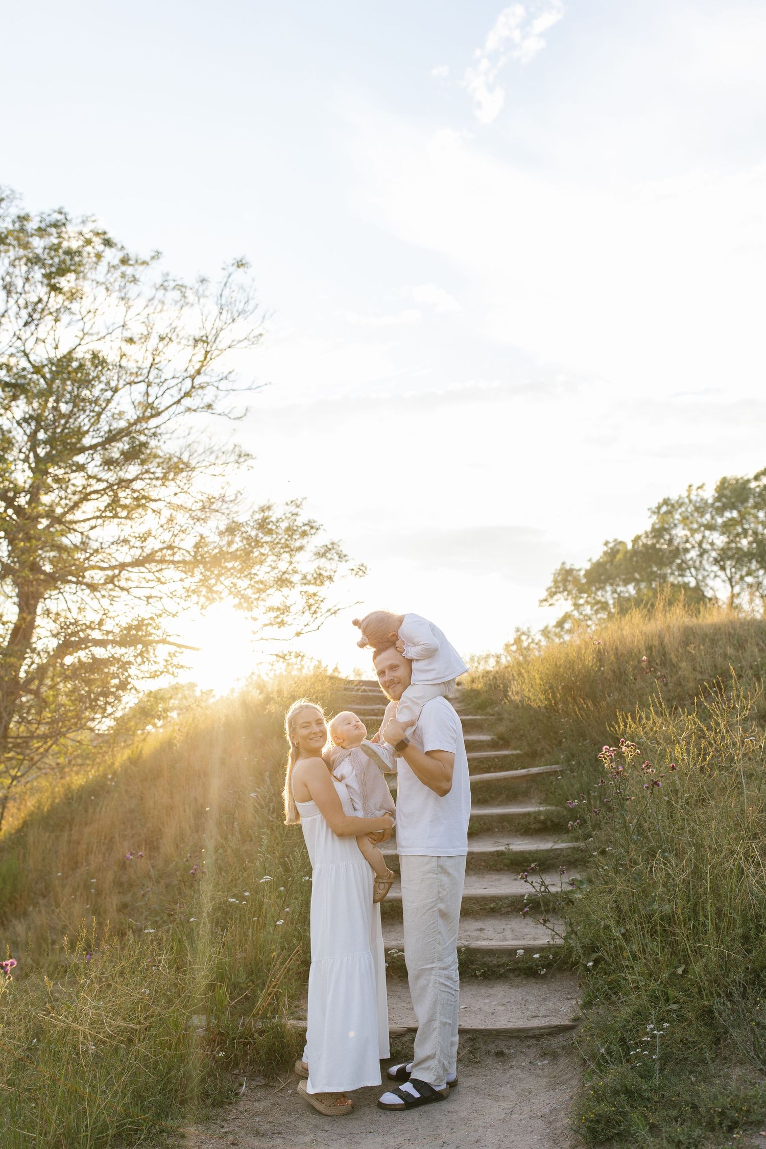 Family in white outfits poses on stone steps during golden sunset.