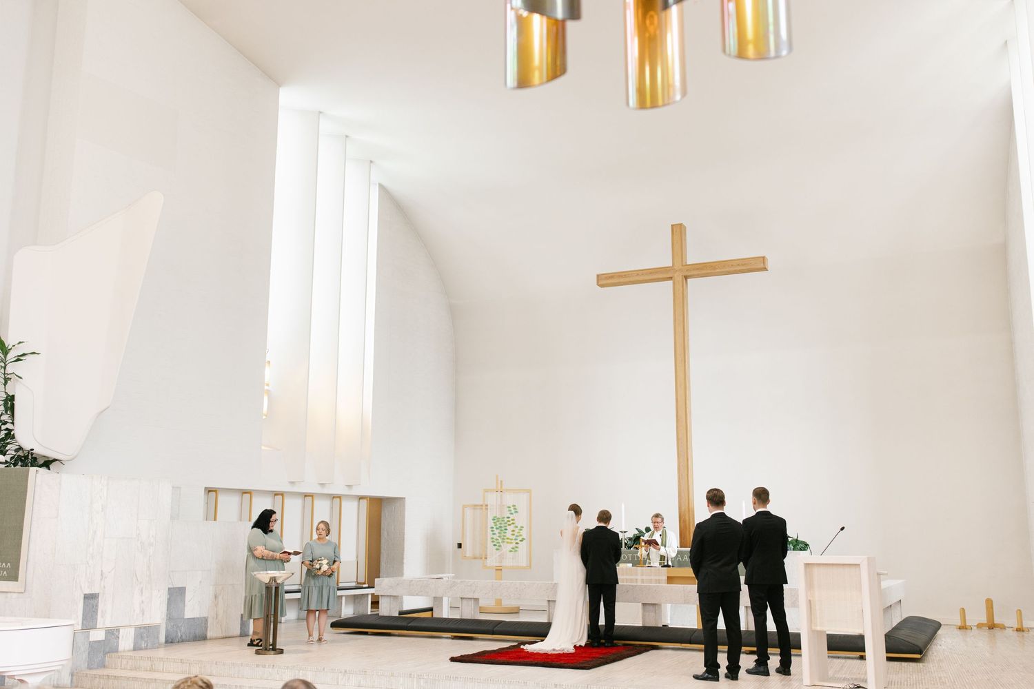 Modern church interior with gold pendant lights and wooden cross for wedding ceremony.